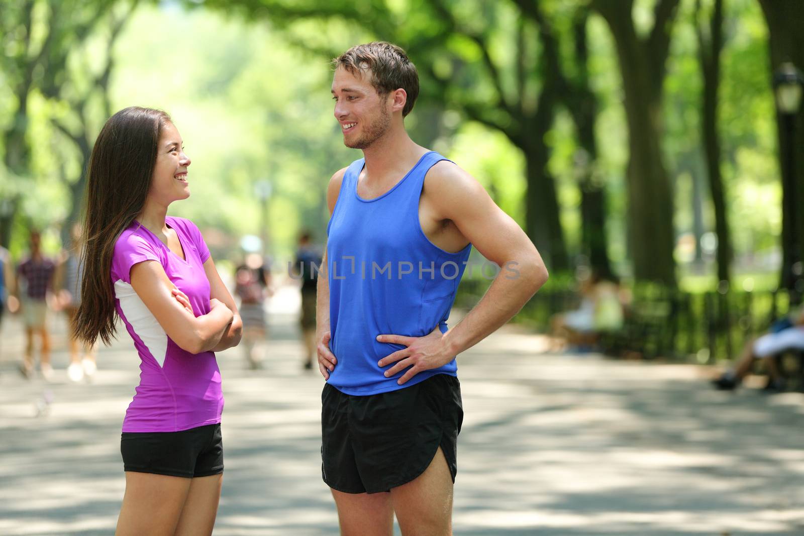 Happy runners couple talking after run in NYC park. Female and male adult athletes resting together in Central Park, New York city, wearing active tops and shorts sportswear for a summer workout.