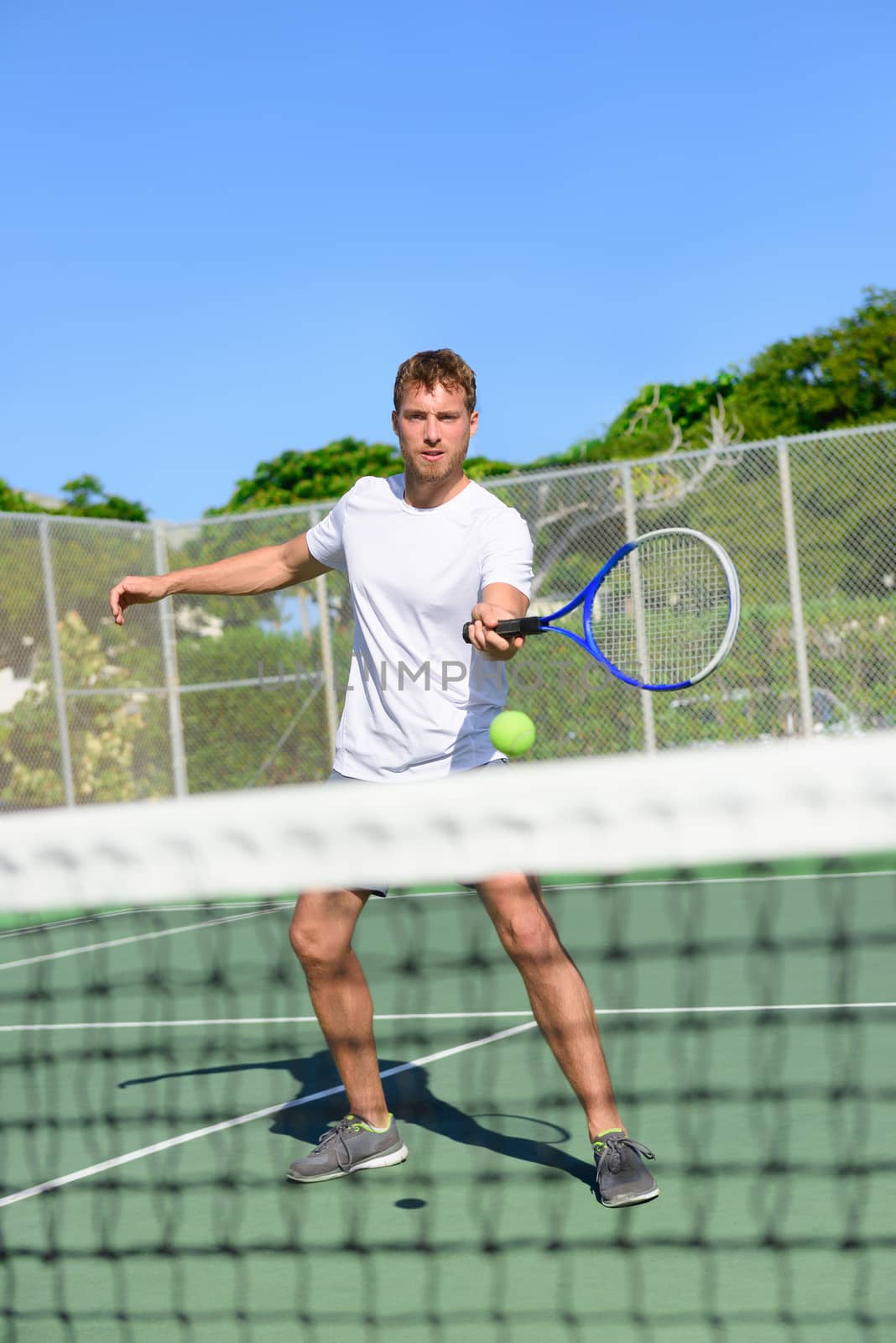 Tennis. Tennis player hitting ball in volley by the net. Male athlete playing outdoors on hard court practicing in summer. Young Caucasian man living healthy active fitness sport lifestyle outside.