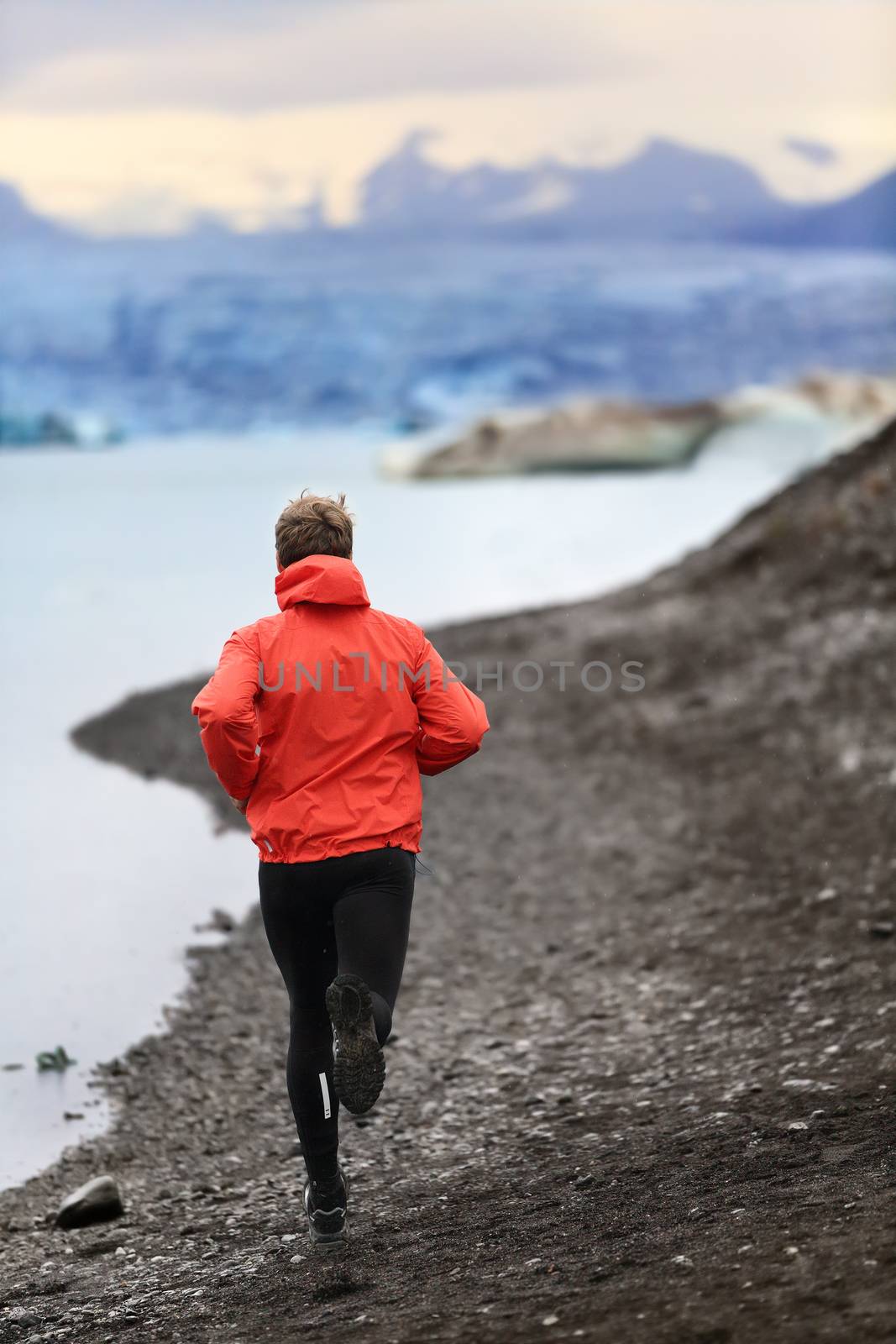 Runner man trail running training for run in beautiful nature landscape. Fit male athlete jogging and cross country running by icebergs in Jokulsarlon glacial lake in Iceland.