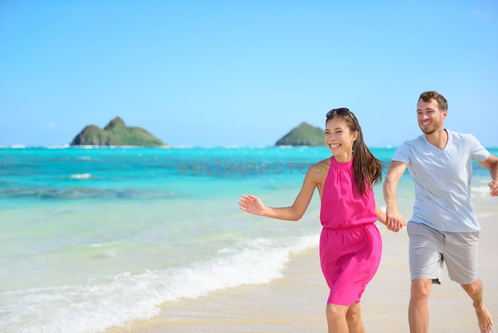 Beach couple happy running having fun on Hawaii. Romantic couple cheerful and full of happiness on travel vacation on Lanikai beach, Oahu, Hawaii, USA with Mokulua Islands. Asian woman, Caucasian man