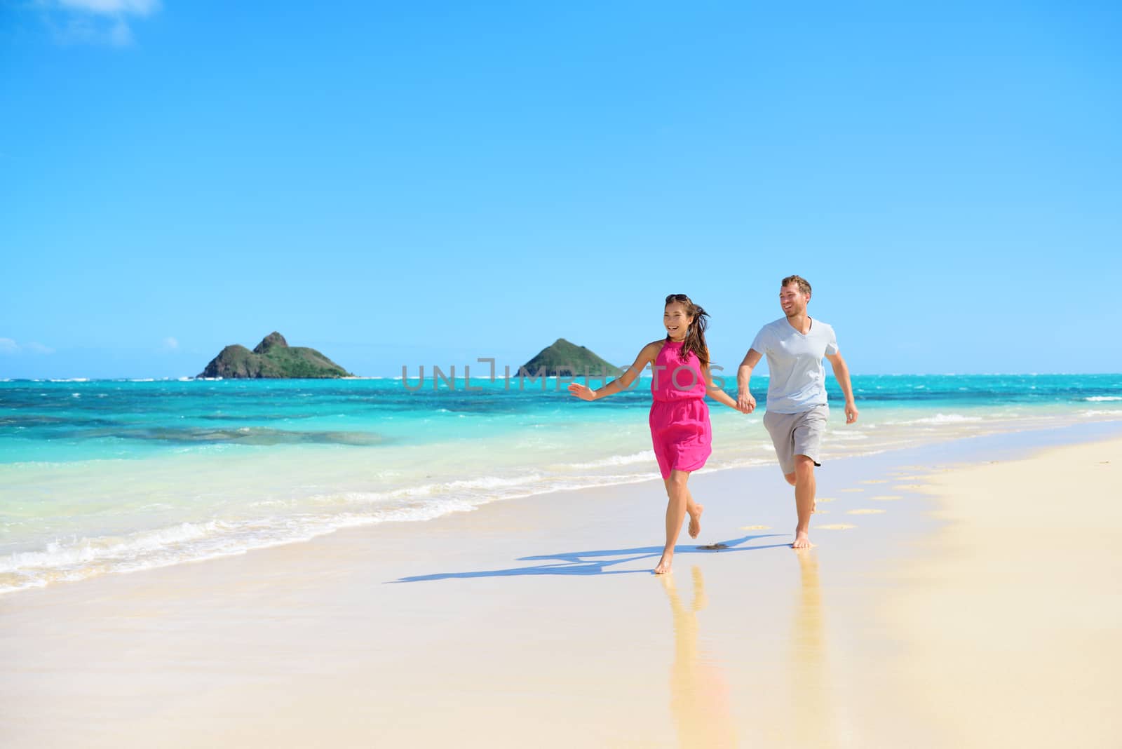 Beach happy couple on running having fun on Hawaii. Romantic couple joyful and full of happiness on travel vacation on Lanikai beach, Oahu, Hawaii, USA with Mokulua Islands. Asian woman, Caucasian man