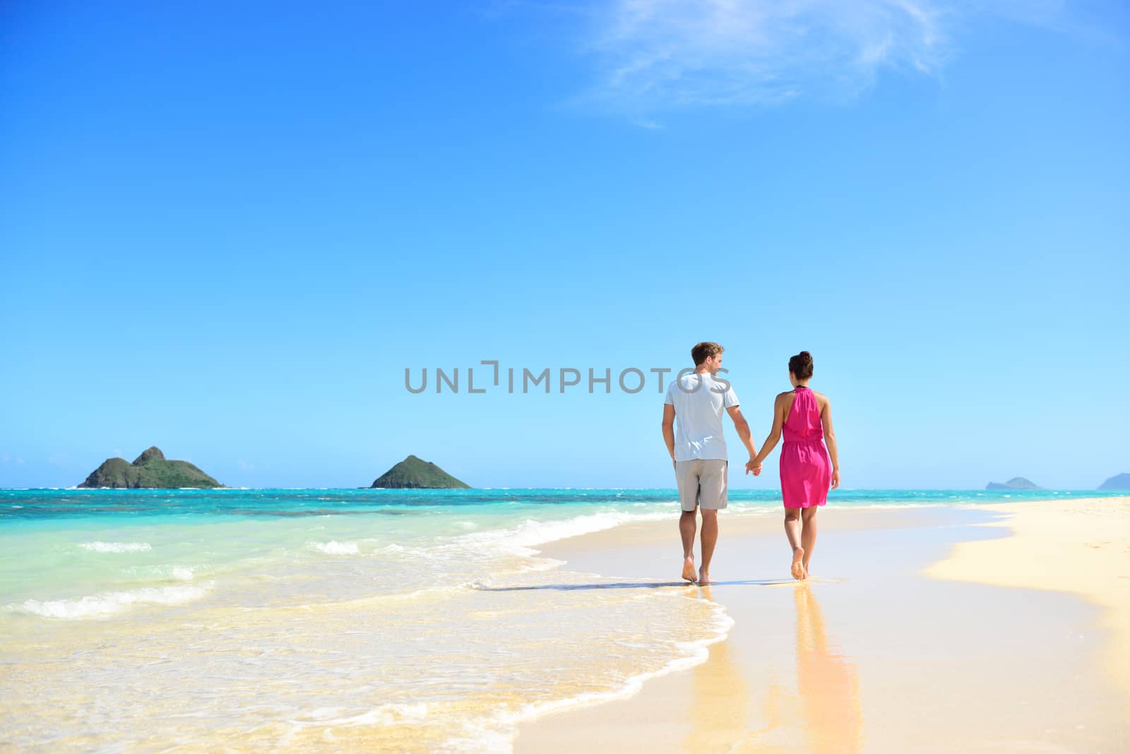 Beach honeymoon couple holding hands walking on white sand beach. Newlyweds happy in love relaxing on summer holidays on Lanikai beach, Oahu, Hawaii, USA with Mokulua Islands. Travel vacation concept.