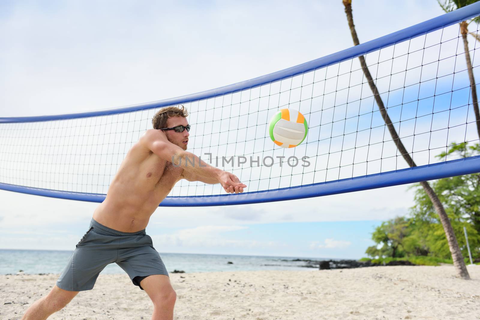 Beach volleyball man playing forearm pass hitting volley ball during game on summer beach. Male model living healthy active lifestyle doing sport on beach.