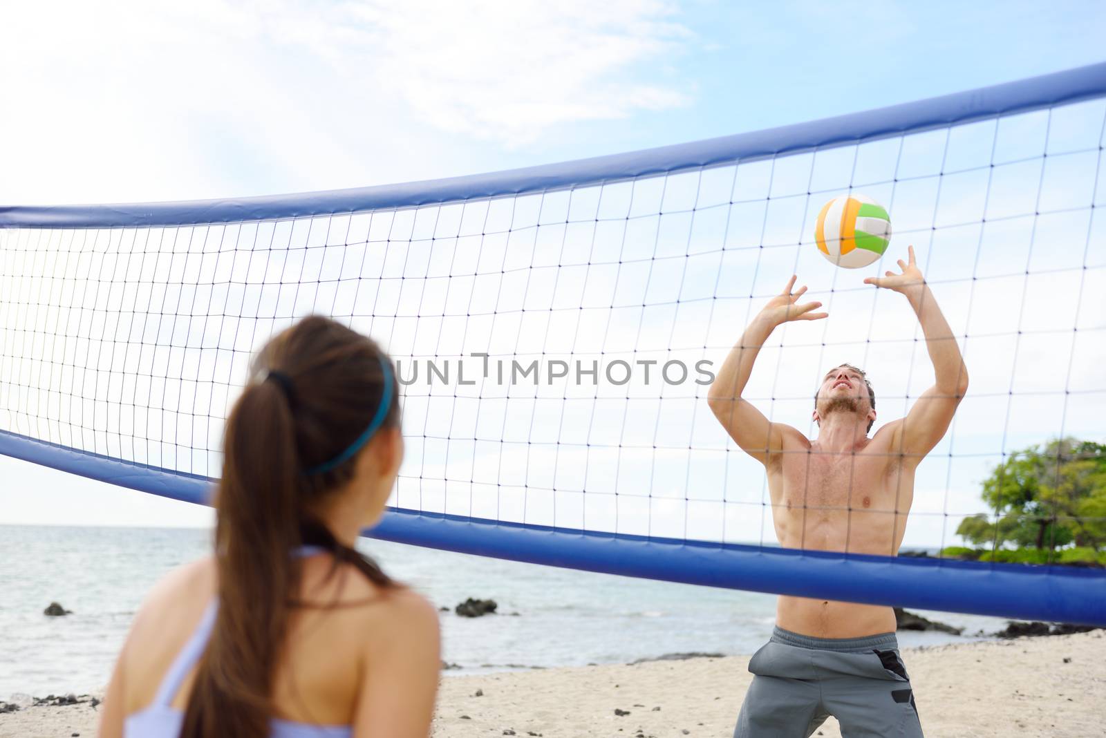People playing beach volleyball having fun in sporty active lifestyle. Man hitting volley ball in game in summer. Woman and man fitness model living healthy lifestyle doing sport on beach.