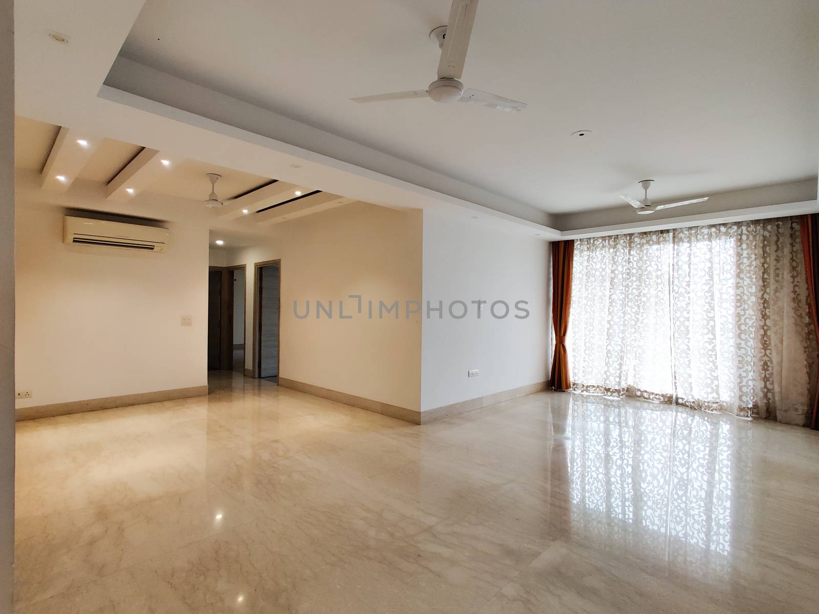 Wide angle shot of a huge apartment with false ceiling lights, curtains on windows polished marble floor. Shot at a modern expensive beautifully maintained flat or apartment in Delhi, Gurgaon, Noida for premium individuals. Shows the real estate of India