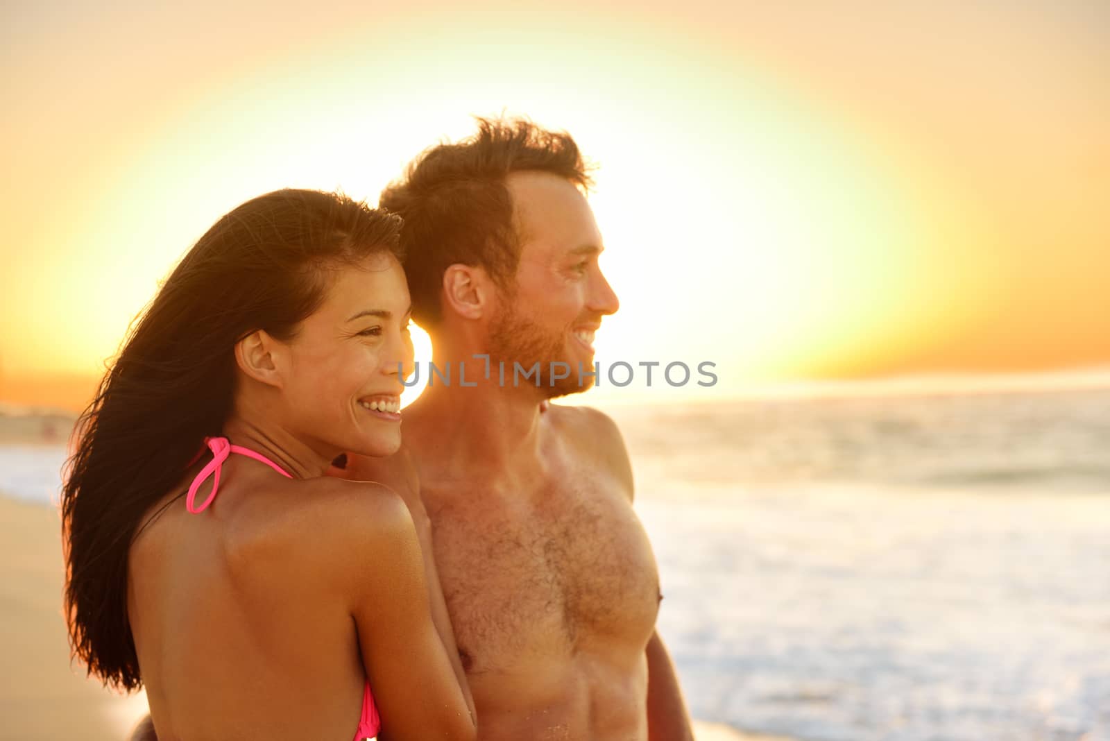 Romantic happy couple lovers on beach honeymoon having playful fun together during summer beach holidays. Cheerful young multiracial couple, Asian woman and Caucasian man. From Oahu, Hawaii, USA.