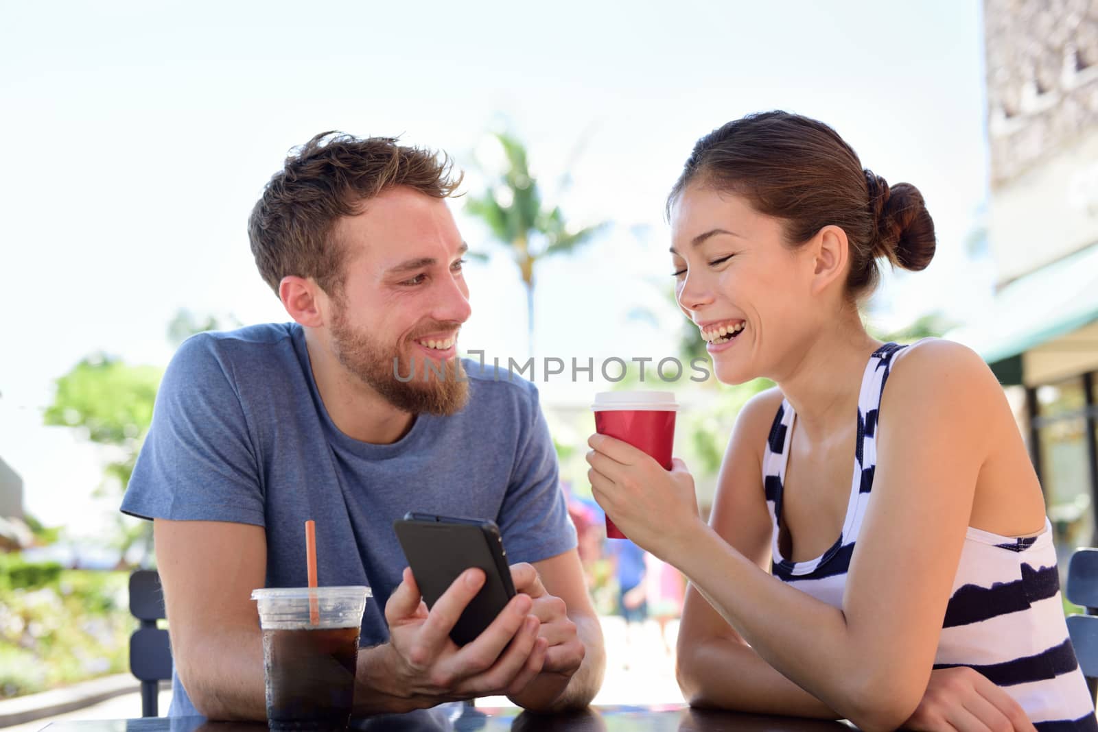 Couple on cafe looking at smart phone app pictures by Maridav