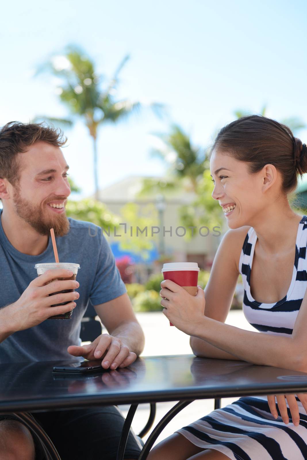 Cafe couple having fun drinking coffee talking smiling and laughing on date in summer. Young man talking with Asian woman sitting outdoors. Happy friends in late 20s.