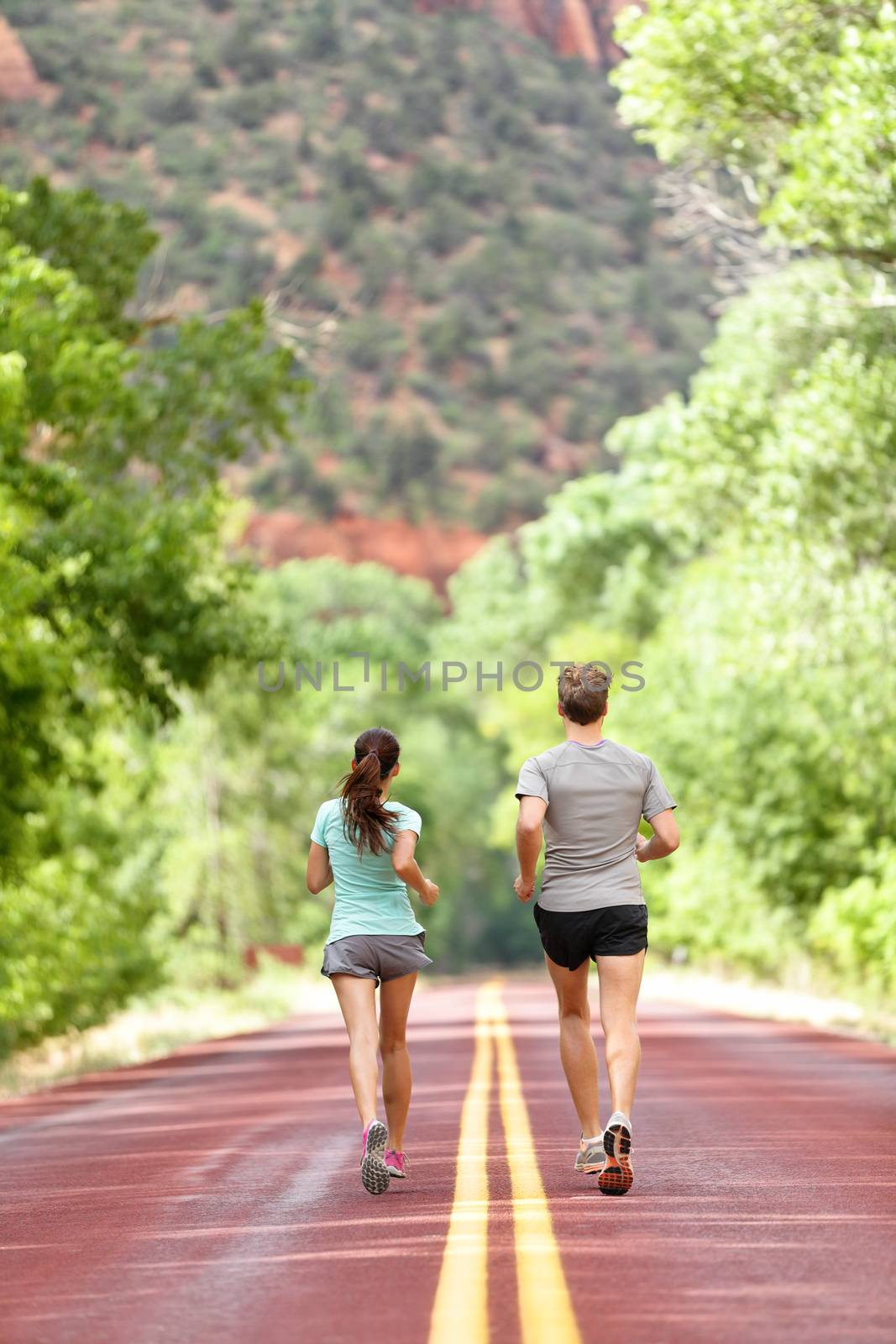 Runners running on road in nature away from camera. Couple, woman and man jogging for a run outside in amazing mountain landscape. Full body length rear view of back. Fitness and healthy lifestyle.