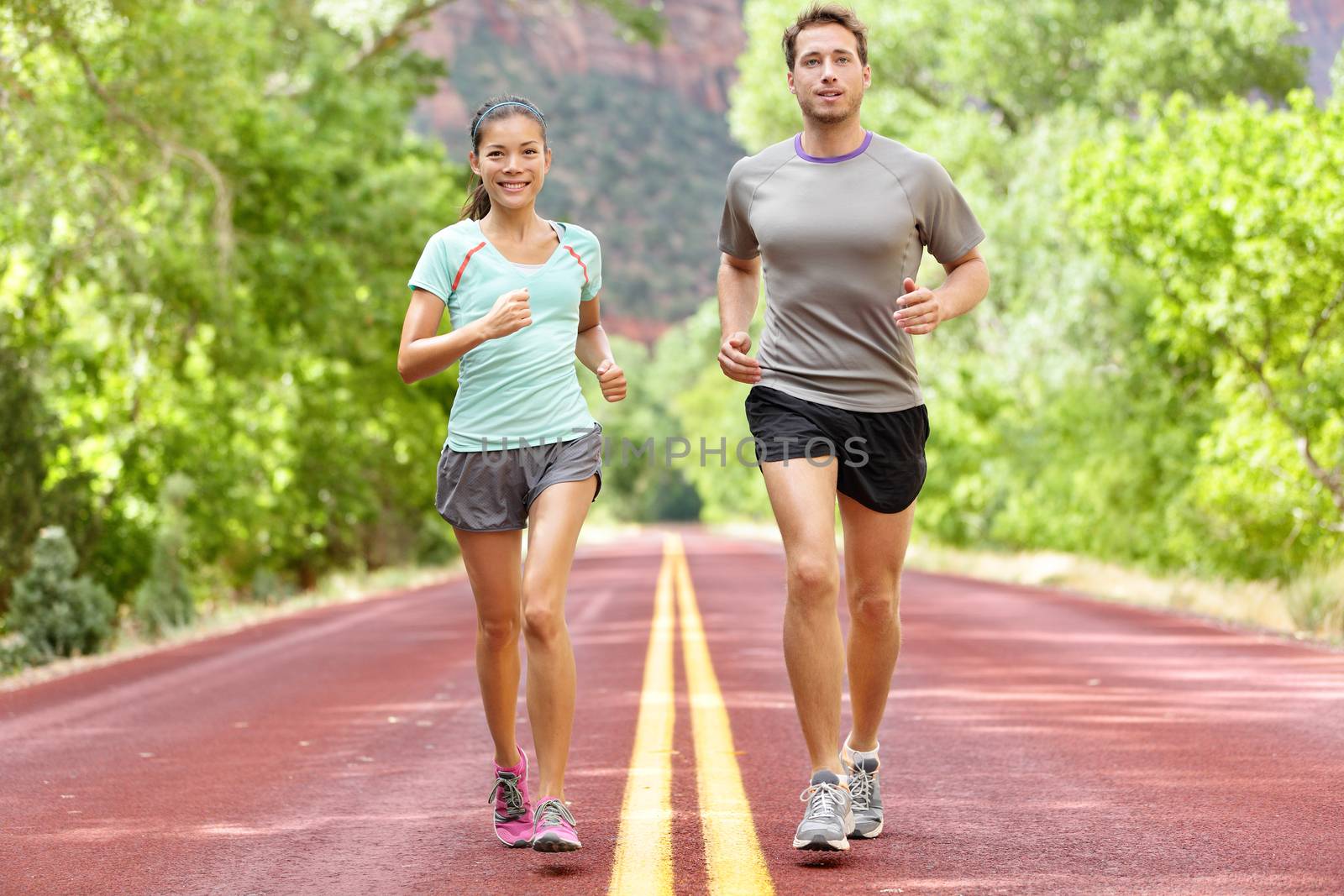 Running Health and fitness. Runners on run training during fitness workout outside on road. People jogging together living healthy active lifestyle outside in summer. Full body length of woman and man