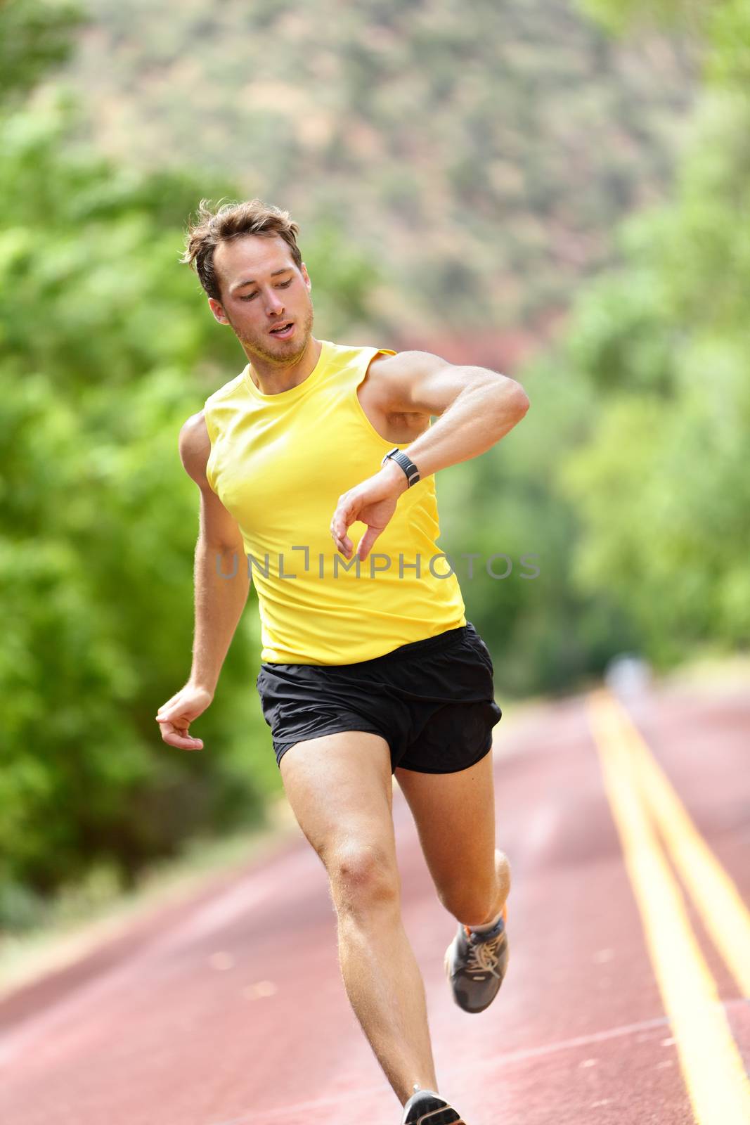 Runner looking at heart rate monitor smart watch while running. Man jogging outside looking at his sports smartwatch during workout training for marathon run. Fit male fitness model in his 20s.