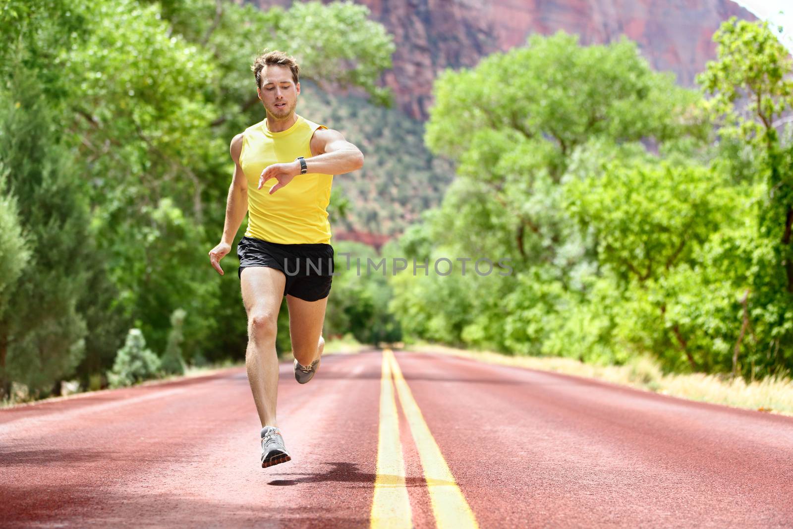 Running man sprinting looking at heart rate monitor smartwatch on run. Man jogging outside looking at his sports smart watch during workout training for marathon. Fit male fitness model in his 20s.