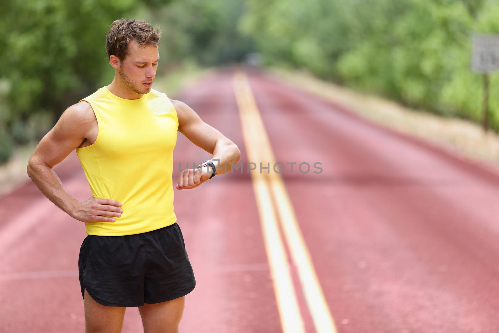 Runner looking at smartwatch heart rate monitor having break while running. Man jogging outside looking at sports smart watch during workout training for marathon. Fit male fitness model in his 20s.