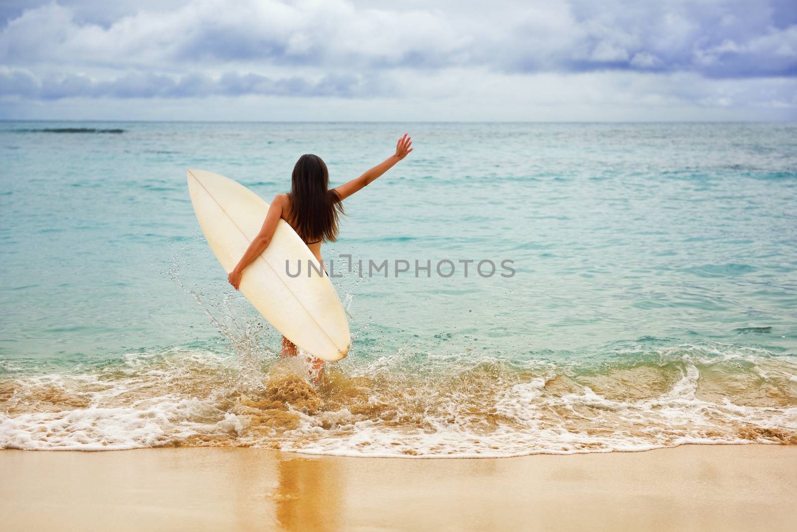 Surfer girl happy cheerful going surfing at ocean beach running into water. Female bikini woman heading for waves with surfboard having fun living healthy active lifestyle by sea.