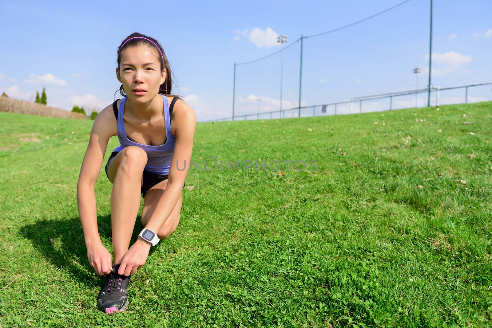 Sporty woman runner preparing for running tying shoe laces in morning on the grass field. Wellness and healthy lifestyle concept with mixed race Asian Caucasian female model going running.