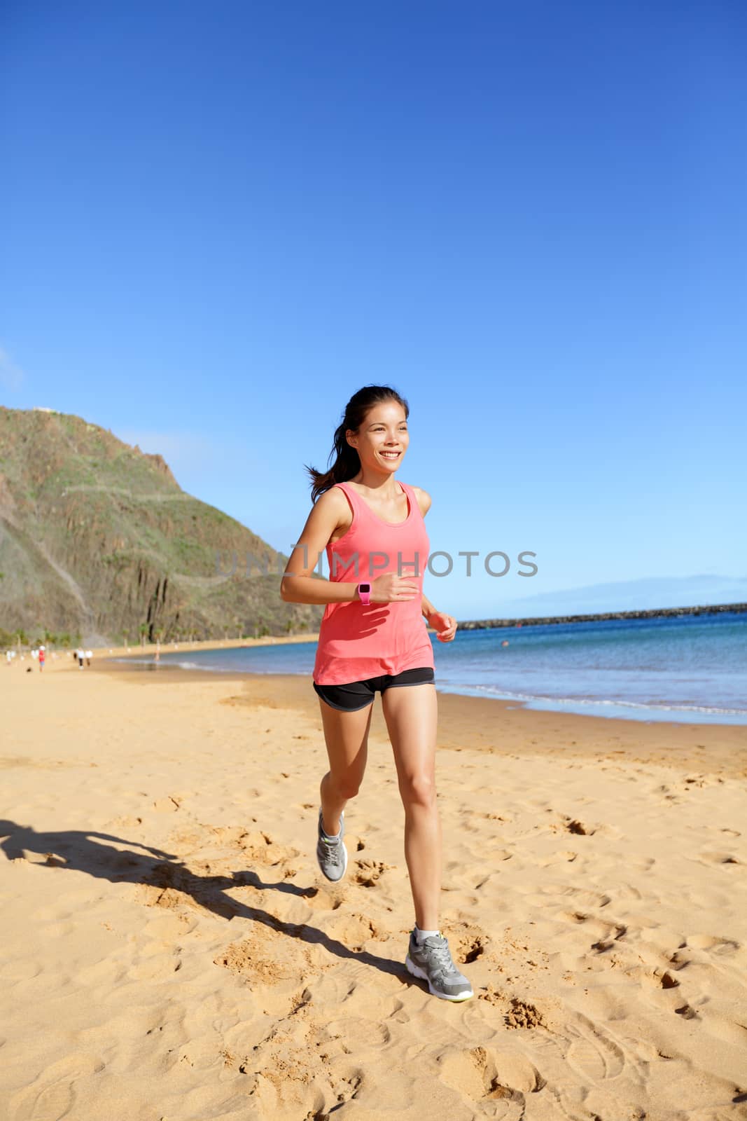 Runner sports athlete running woman on beach sweating and jogging. Fit exercising female fitness model working out training for marathon run. Biracial Asian Caucasian sports girl.