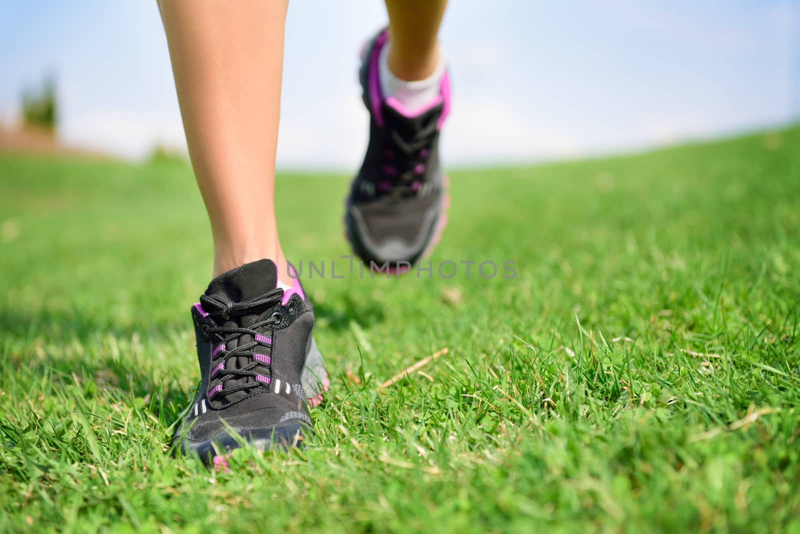 Runner athlete feet running on grass. Fitness woman jog workout and wellness concept. Close up of female running shoes and legs.
