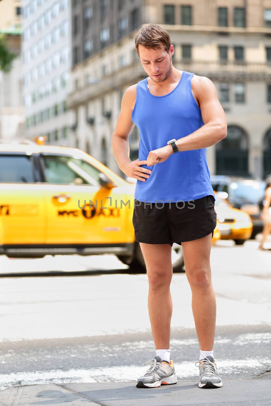 Runner looking at smartwatch heart rate monitor having break while running in New York City, Manhattan. Man jogging outside looking at sports smart watch training for marathon. Male fitness model