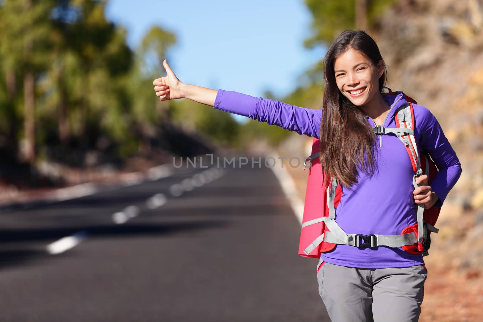 Travel hitchhiker woman backpacking hitchhiking thumbing happy walking on road side during holiday travel. Beautiful outdoors woman model. Mixed race Asian Caucasian