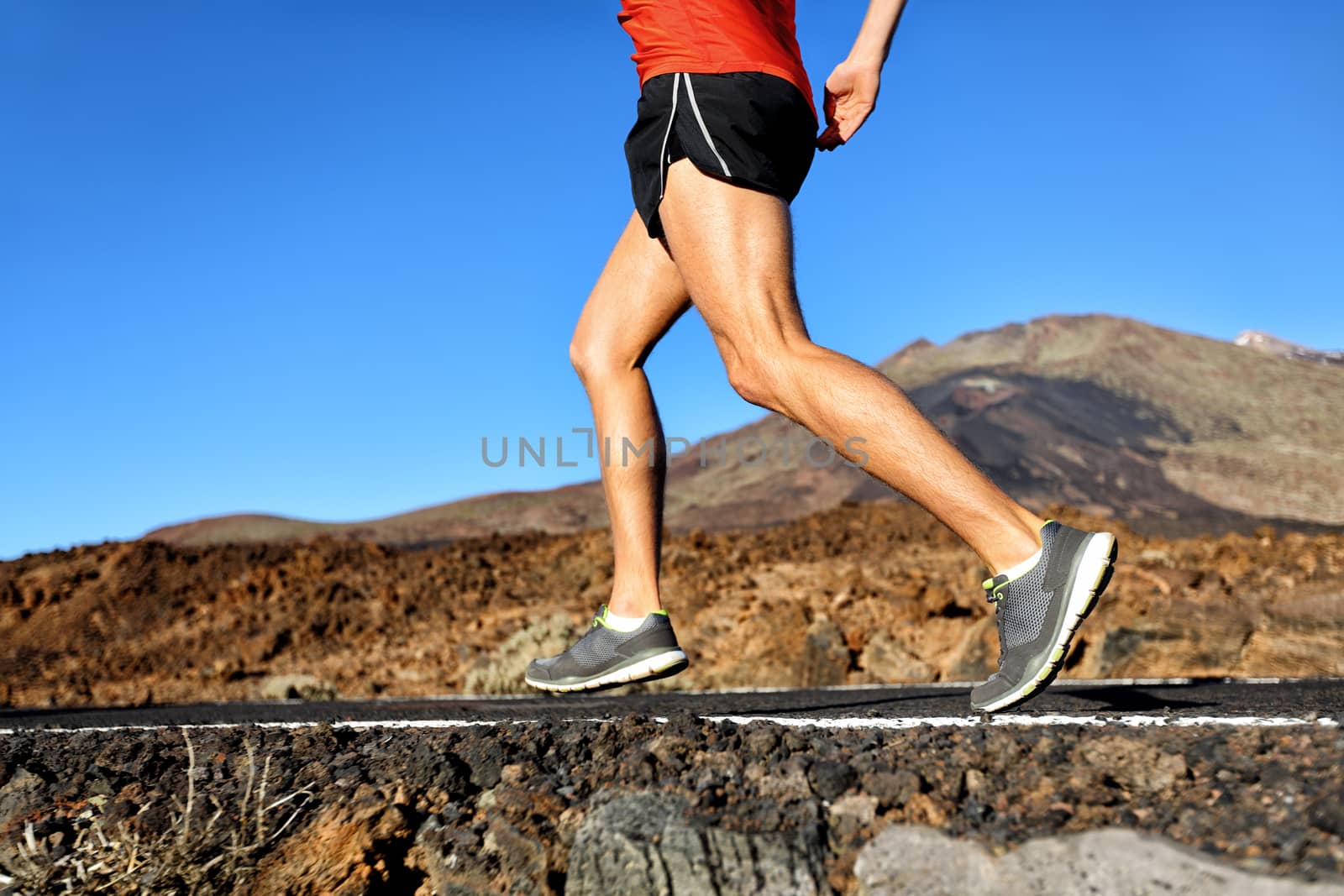 Running athlete man runner jogging on nature road in forest mountain. Lower half body running shoes and legs of male adult on a jog in summer.