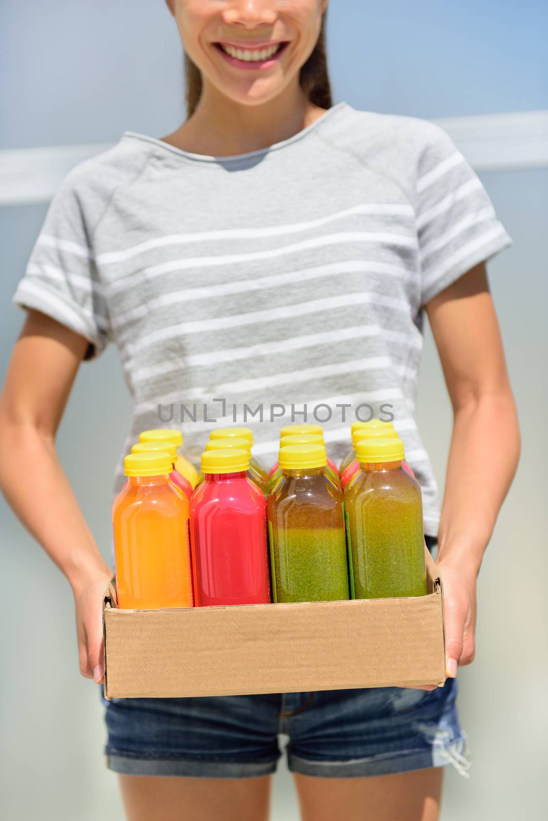 Juice detox - cleanse diet with juicing raw and organic fruits and veggies. Fresh juices delivery woman with vegetable drinks. Young girl carrying a box of juice bottles.