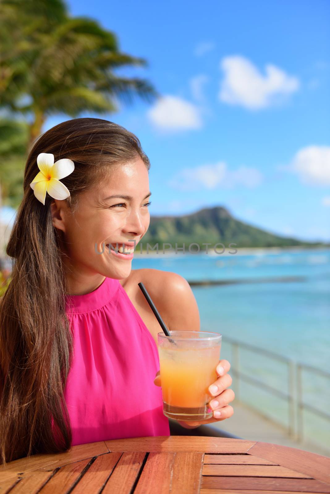 Cocktail woman drinking alcohol drinks at beach bar resort in Waikiki, Honolulu city, Oahu, Hawaii, USA. Asian girl tourist looking at camera toasting a glass of strawberry Hawaiian drink at sunset.