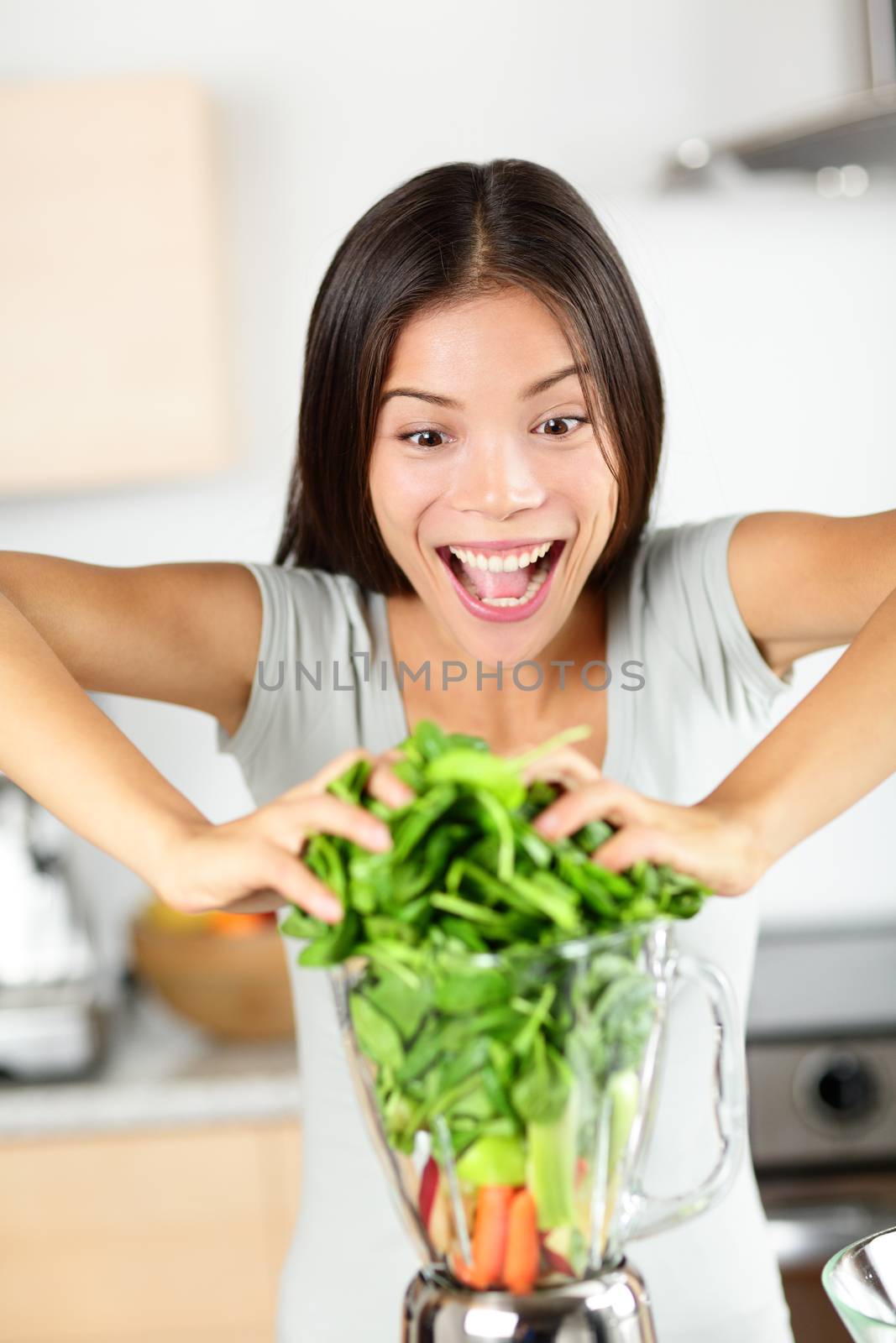 Vegetable smoothie woman making green smoothies with blender home in kitchen. Funny healthy raw eating lifestyle concept portrait of beautiful young woman preparing drink with spinach, carrots