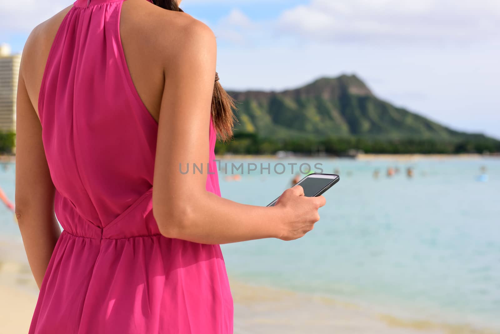 Smart phone woman using smartphone app on Waikiki Beach. Girl sms text messaging or browsing on internet outdoors. Close up of mobile phone and model hands on Oahu, Hawaii, USA.