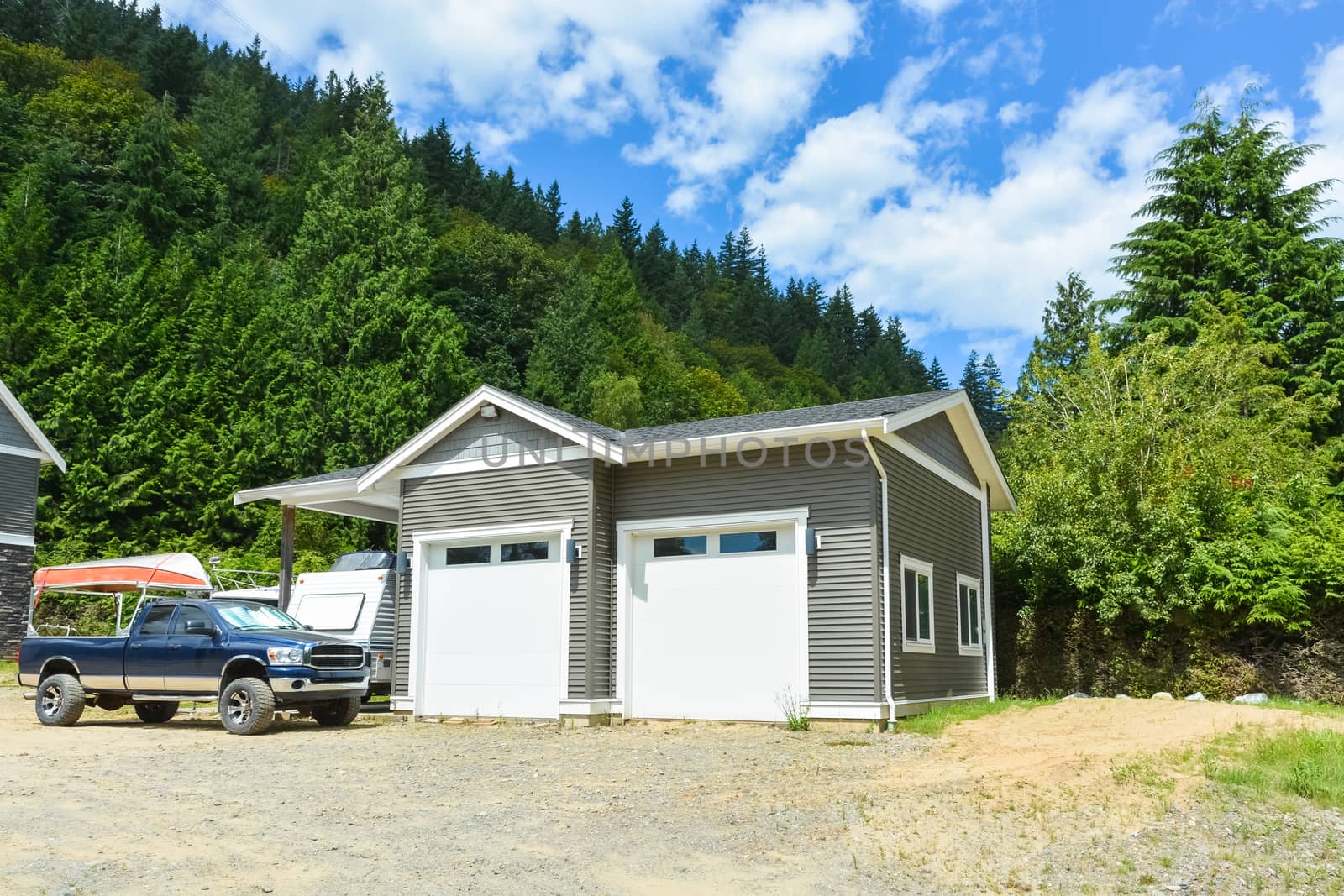 Brand new family house with car and boat parked on gravel driveway. New residential house and detached double garage on country side in British Columbia, Canada