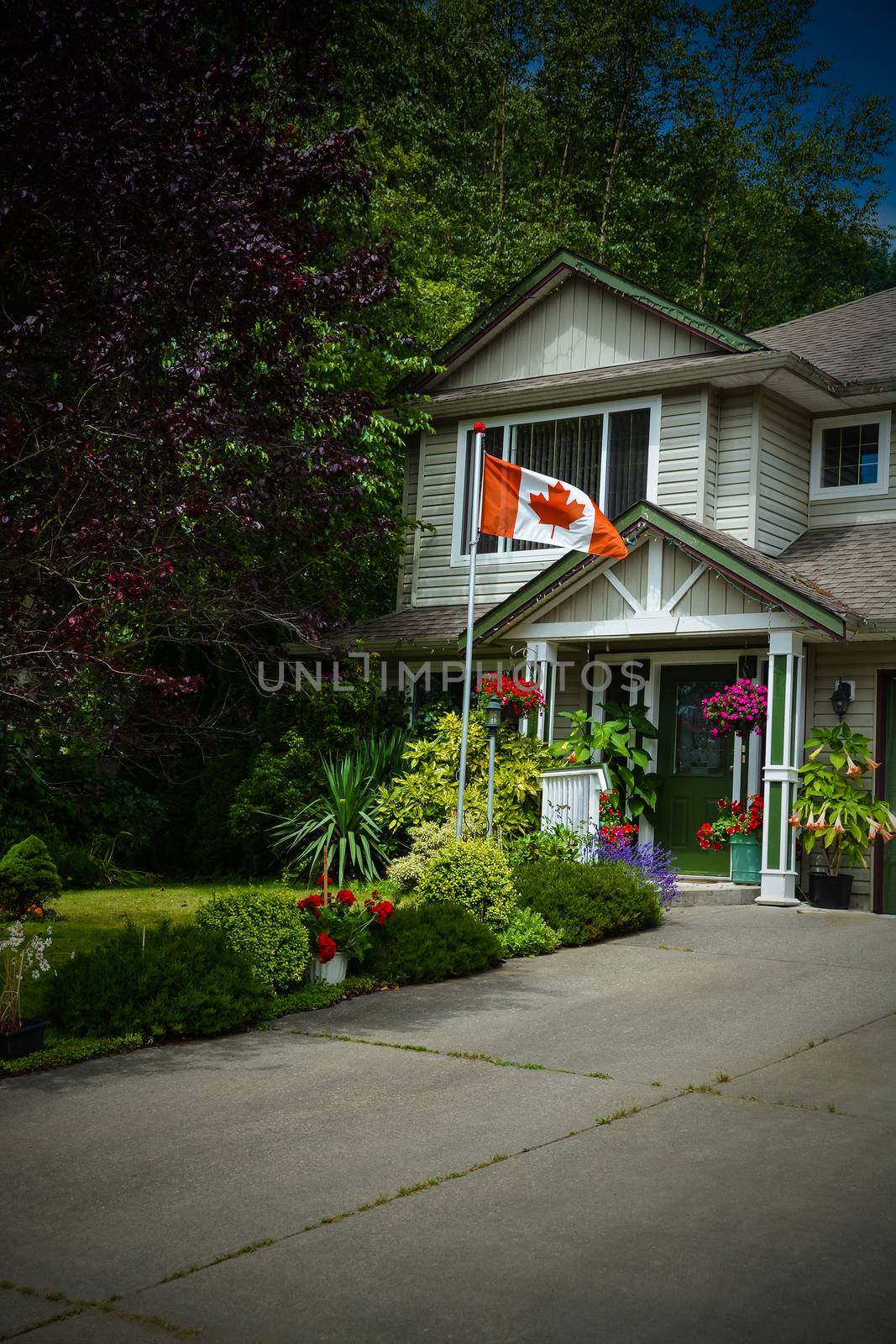 Main entrance of family house with canadian flag in front. Fragment of residential house with concrete driveway. Image with dark borders