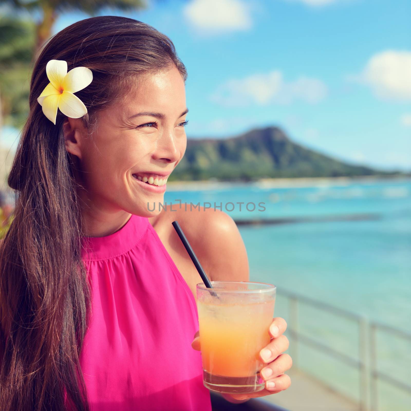 Happy young woman holding cocktail glass at beach bar. Beautiful mixed race Asian / Caucasian female is looking away while enjoying summer vacation having refreshment spending leisure time at beach.
