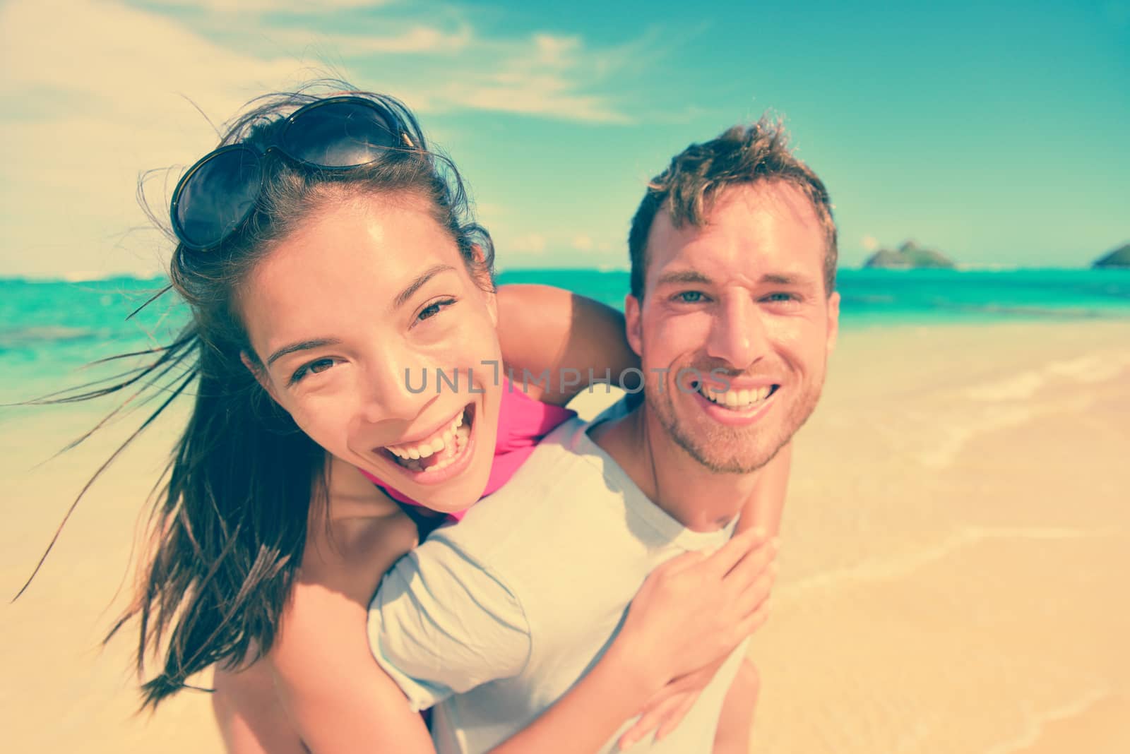 Portrait of happy young man giving piggyback ride to woman at beach. Excited couple are enjoying their summer vacation. Multiethnic tourists are having fun on shore.