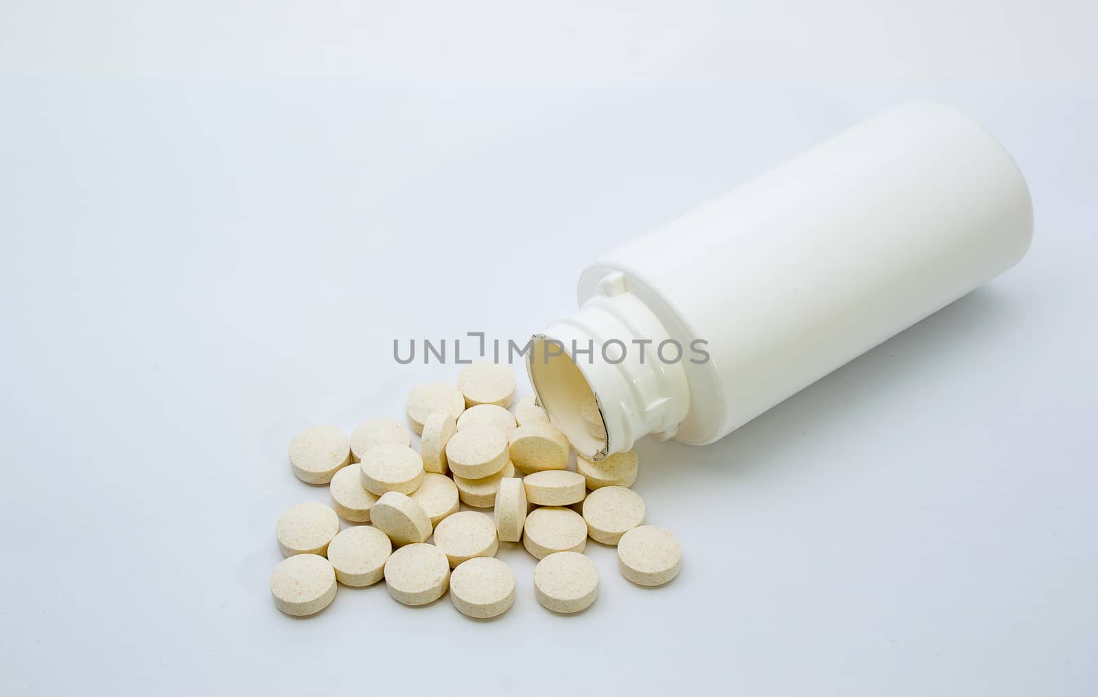 Vitamin tablets spilt from a white bottle and shown on a white background