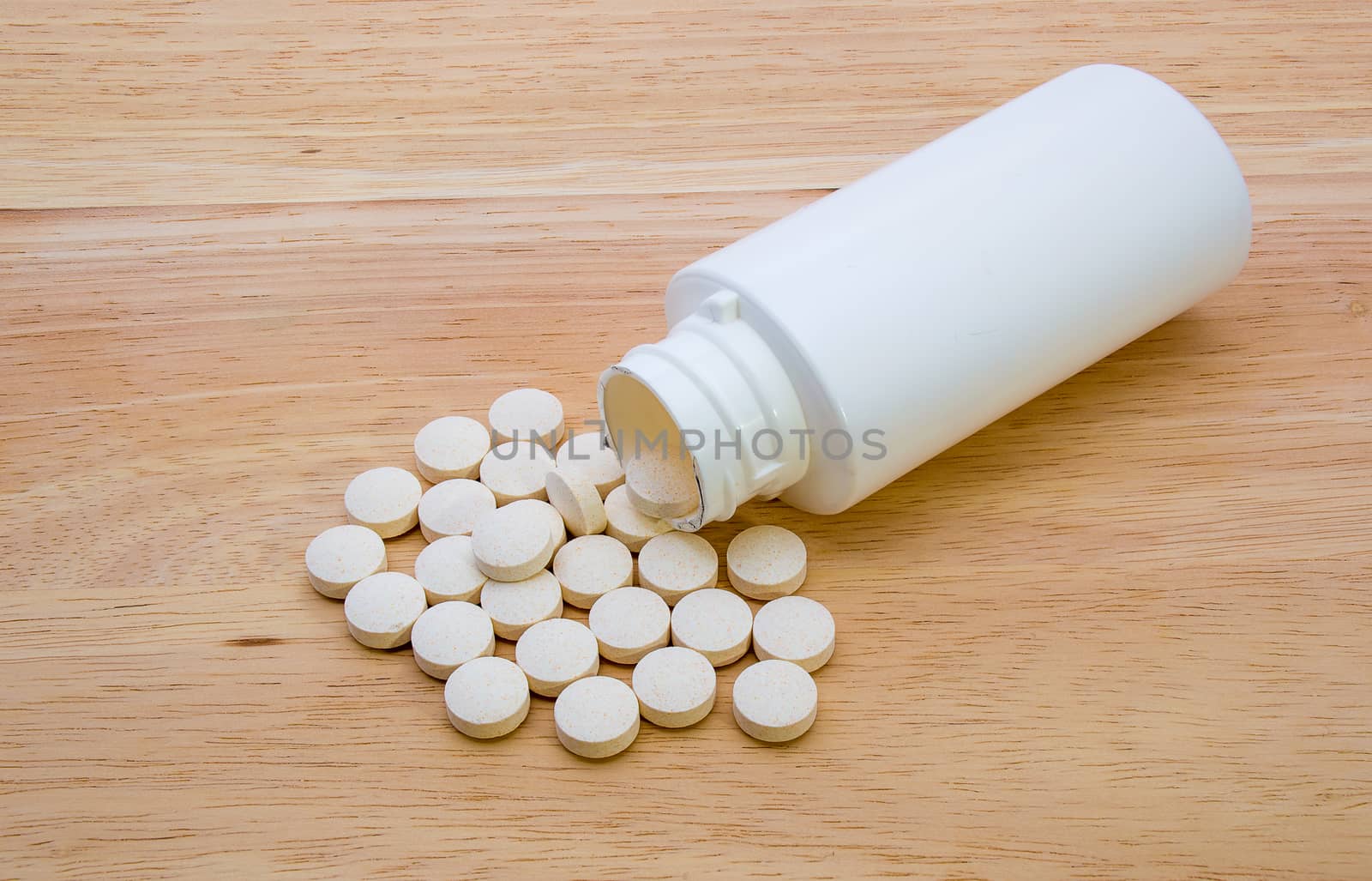 Vitamin tablets spilt from a white bottle and shown on a wooden background