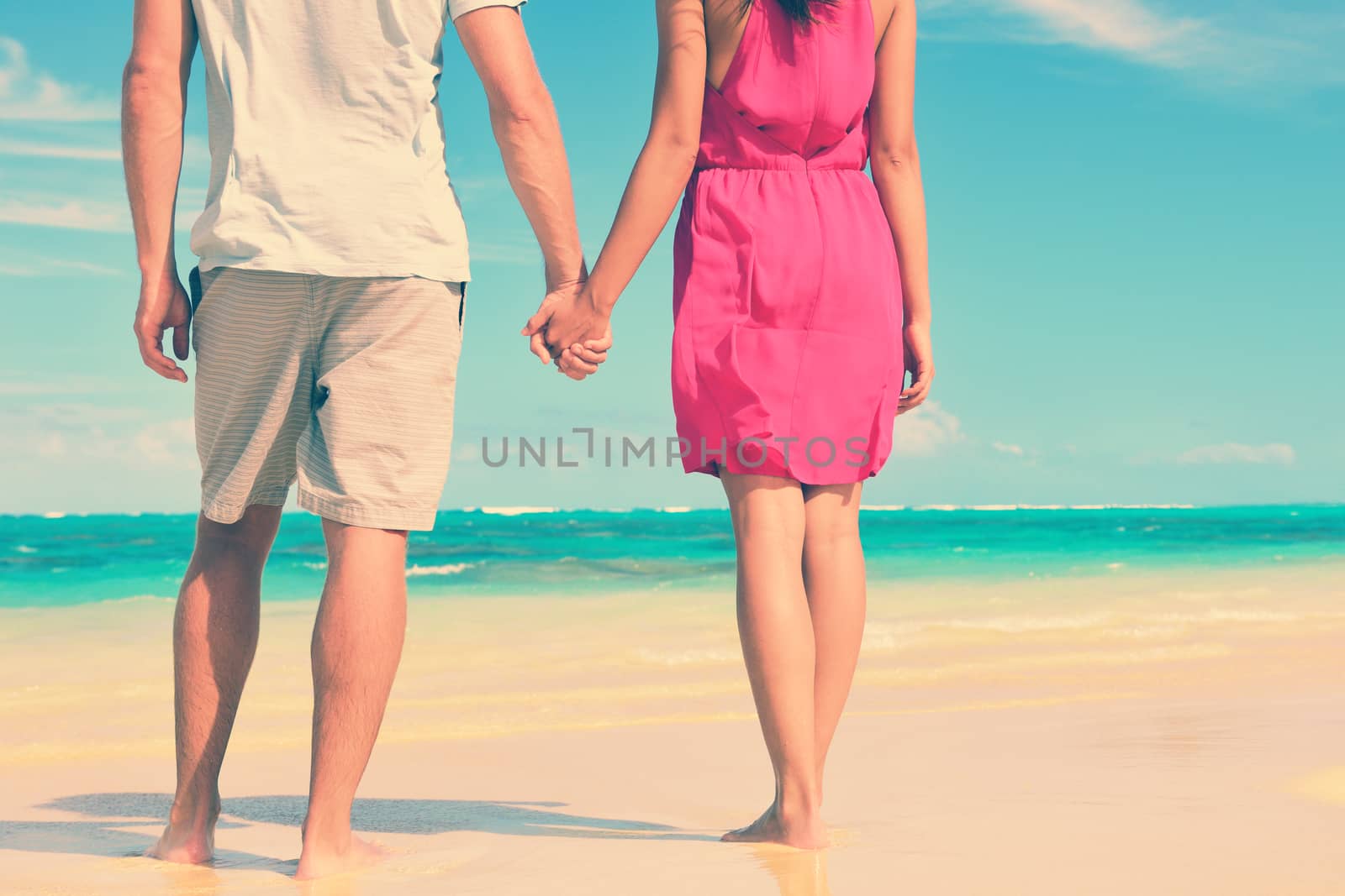 Low section of multiethnic couple holding hands on shore. Loving young tourists are standing at beach. They are spending leisure time together.
