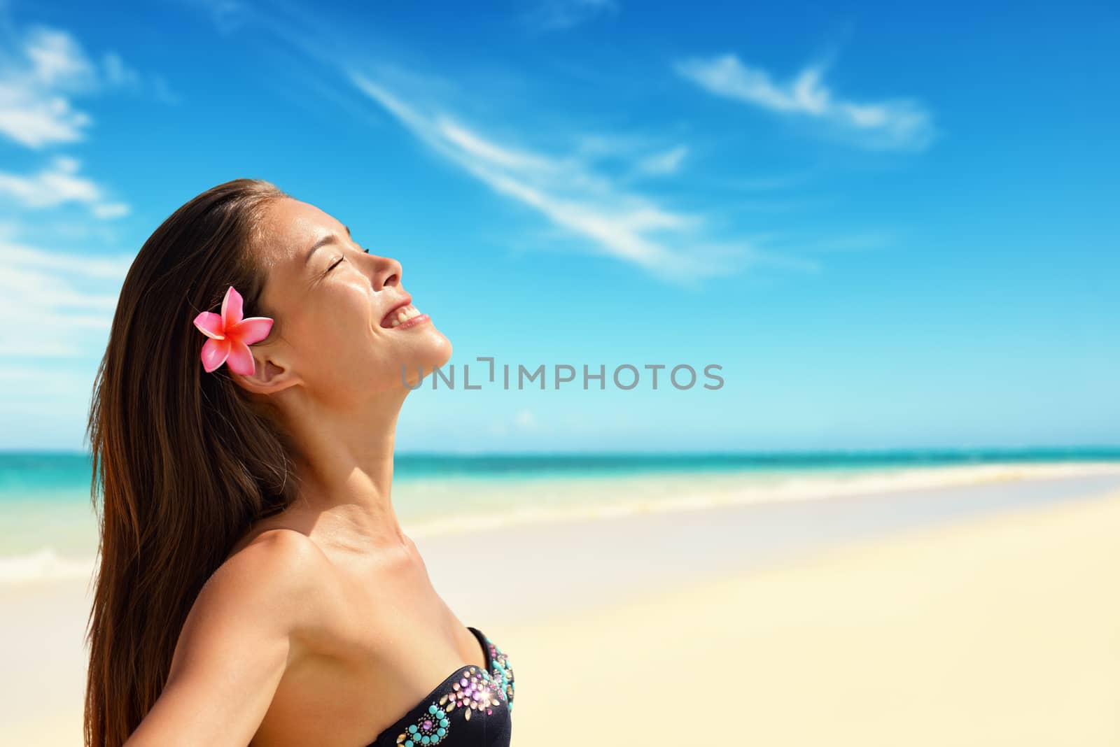 Happy beautiful woman wearing flower while enjoying sunlight at beach. Mixed race Asian / Caucasian female is with eyes closed. She is on summer vacation.