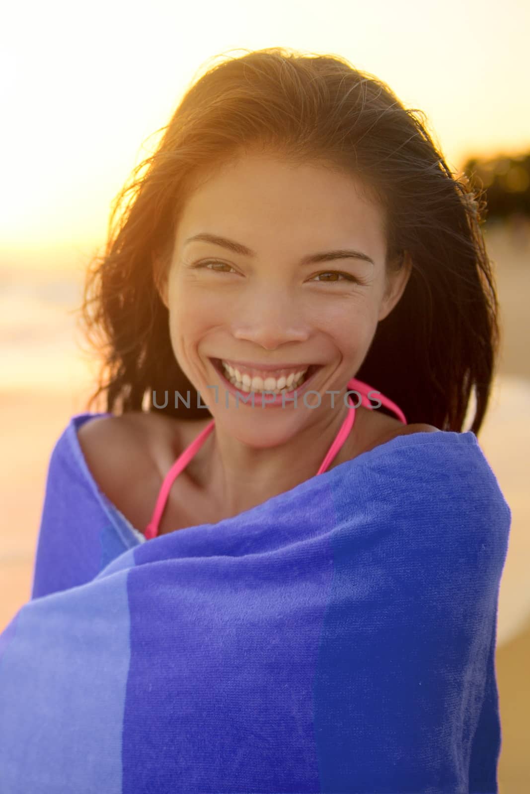 Portrait of happy young woman wrapped in towel drying after swimming in ocean on beach. Beautiful mixed race Asian / Caucasian female is at beach. She is enjoying her summer vacation.