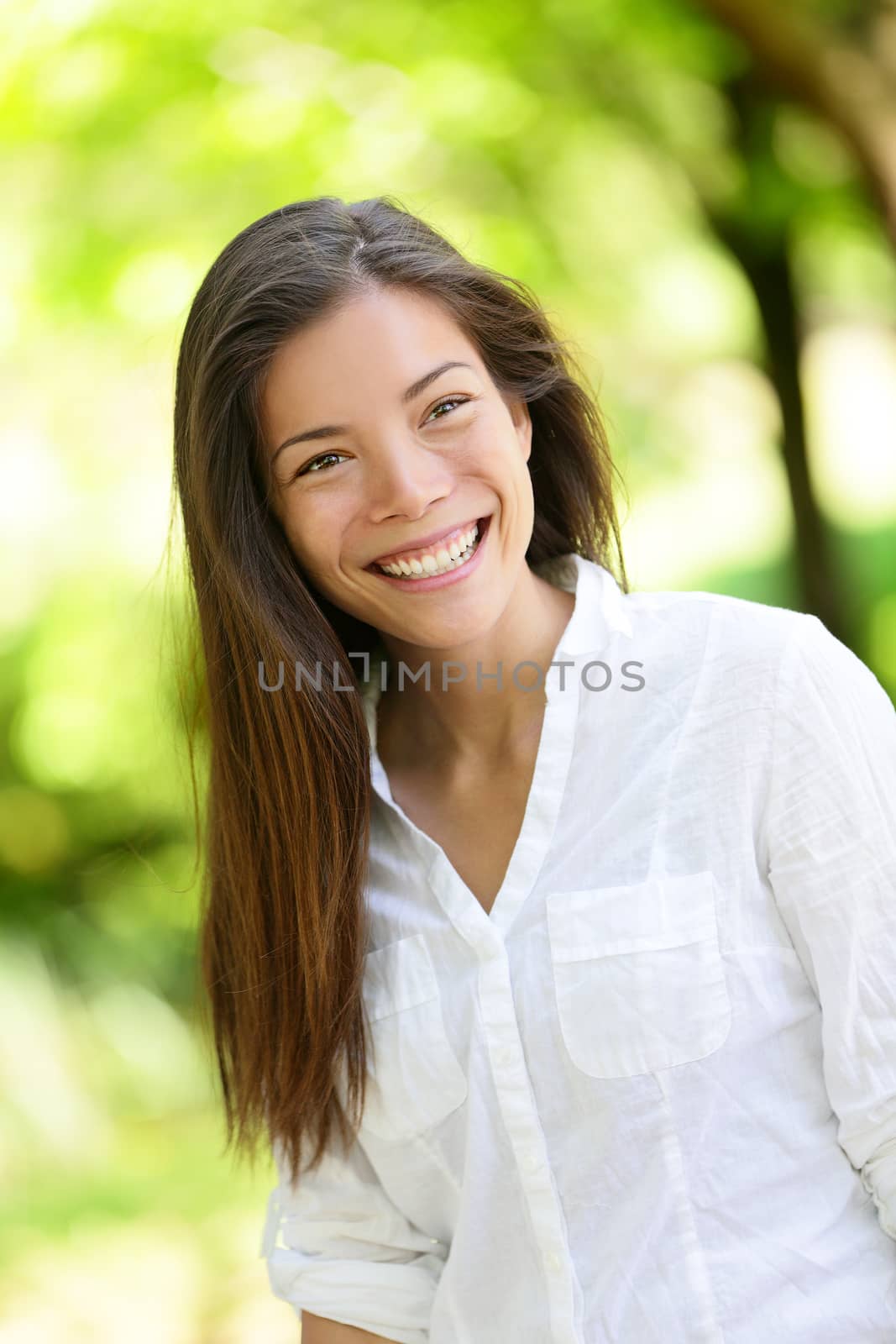 Beautiful happy young woman looking away. She is with long brown hair. Mixed race Asian / Caucasian female is in casuals at park.