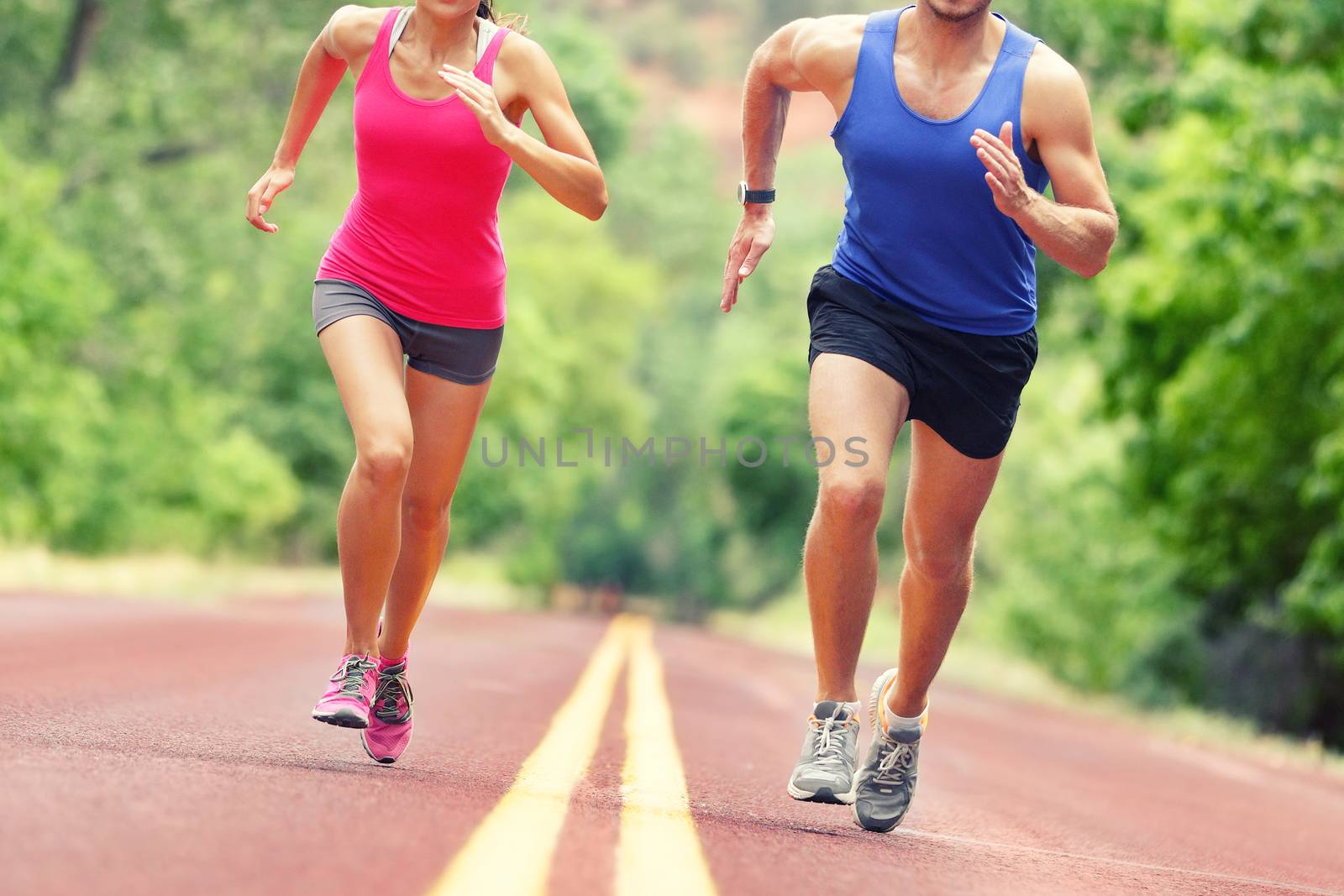 Low section of determined man and woman running on country road. Young couple is in sports clothing. They are representing their healthy lifestyle.