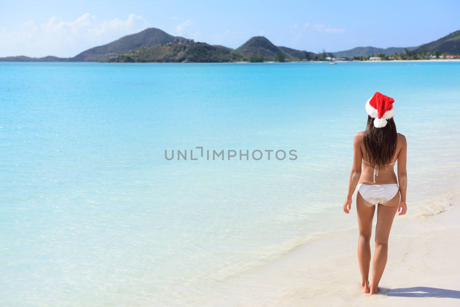 Woman in Santa hat on beach travel vacation getaway enjoying view of tropical beach turquoise paradise beach in the Caribbean. Beautiful girl in bikini under the sun.