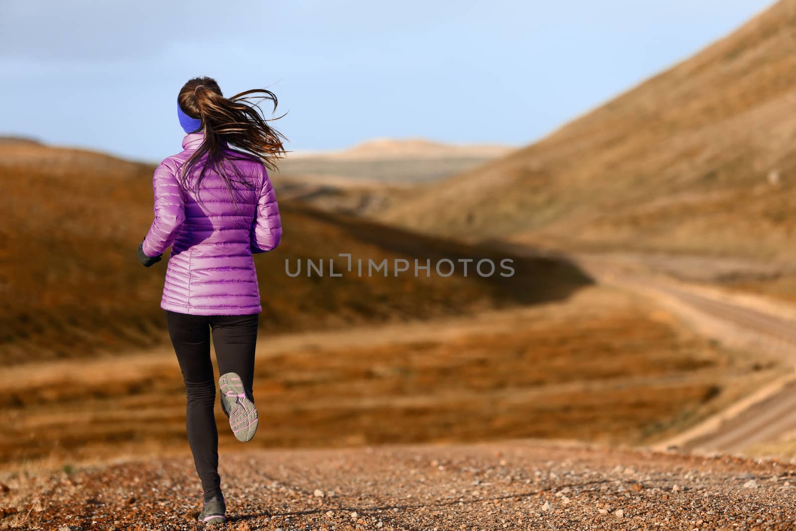 Woman trail runner running in mountain landscape. Female runner in warm clothes for autumn jogging cross country outdoors in foliage nature background.