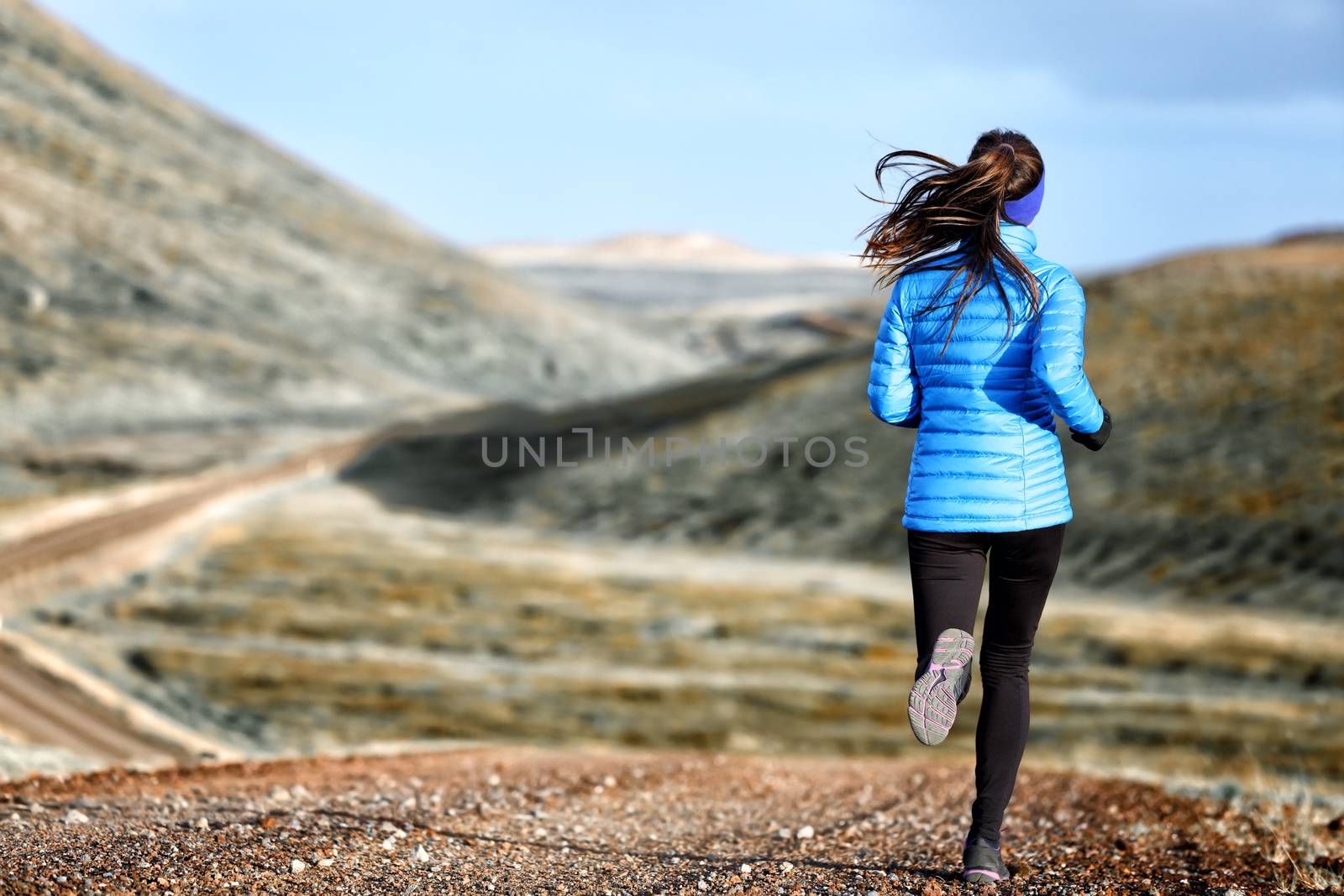 Woman winter and autumn running in down jacket. Female running jogging on mountain trail in beautiful landscape.