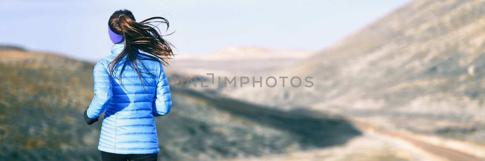 Winter running woman on trail run outdoors in snowy mountains background. Panoramic banner with copy space on white snow.