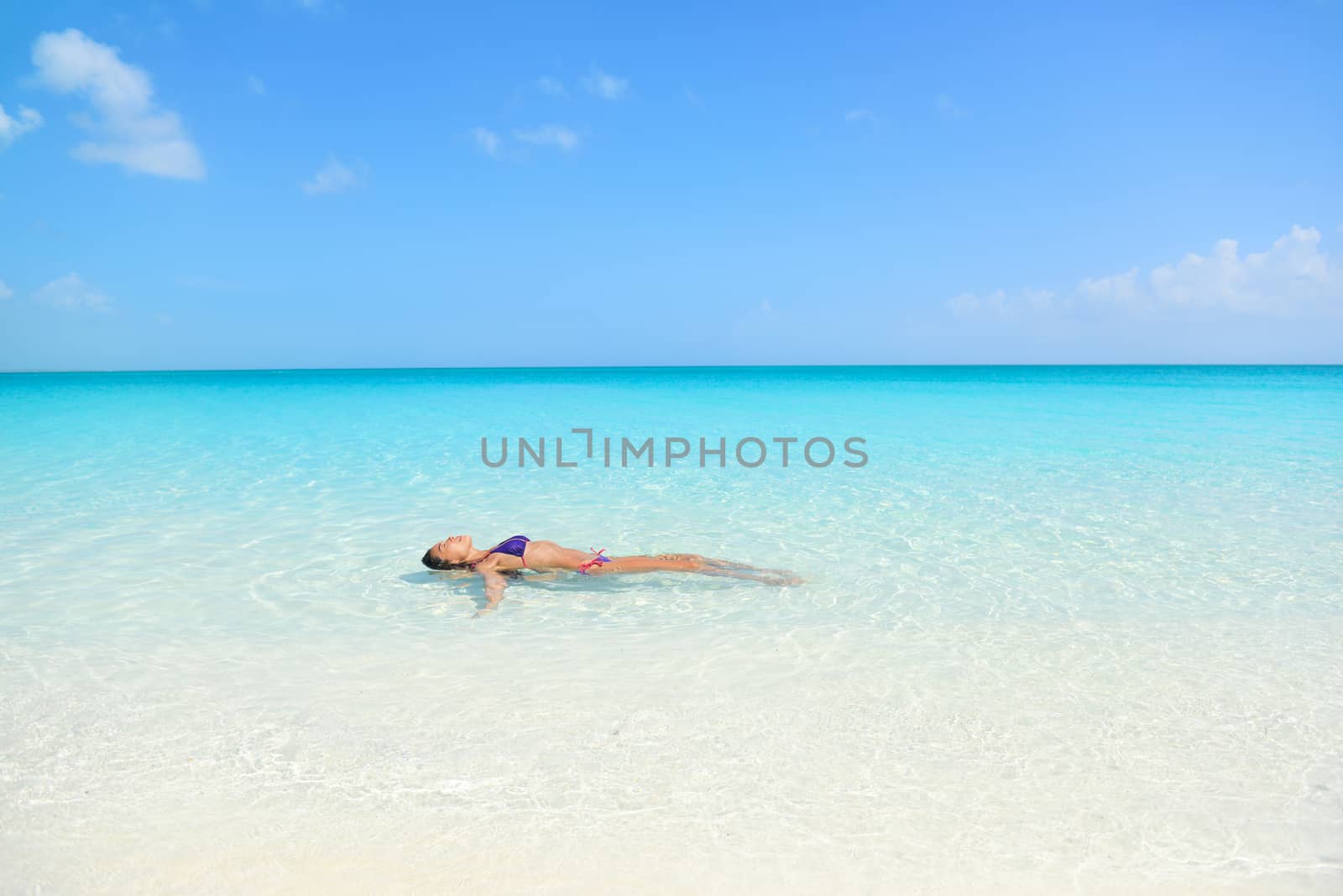 Woman swimming in ocean relaxing enjoying the sun bathing in peaceful blue water. Sexy female adult floating meditating in the sea.