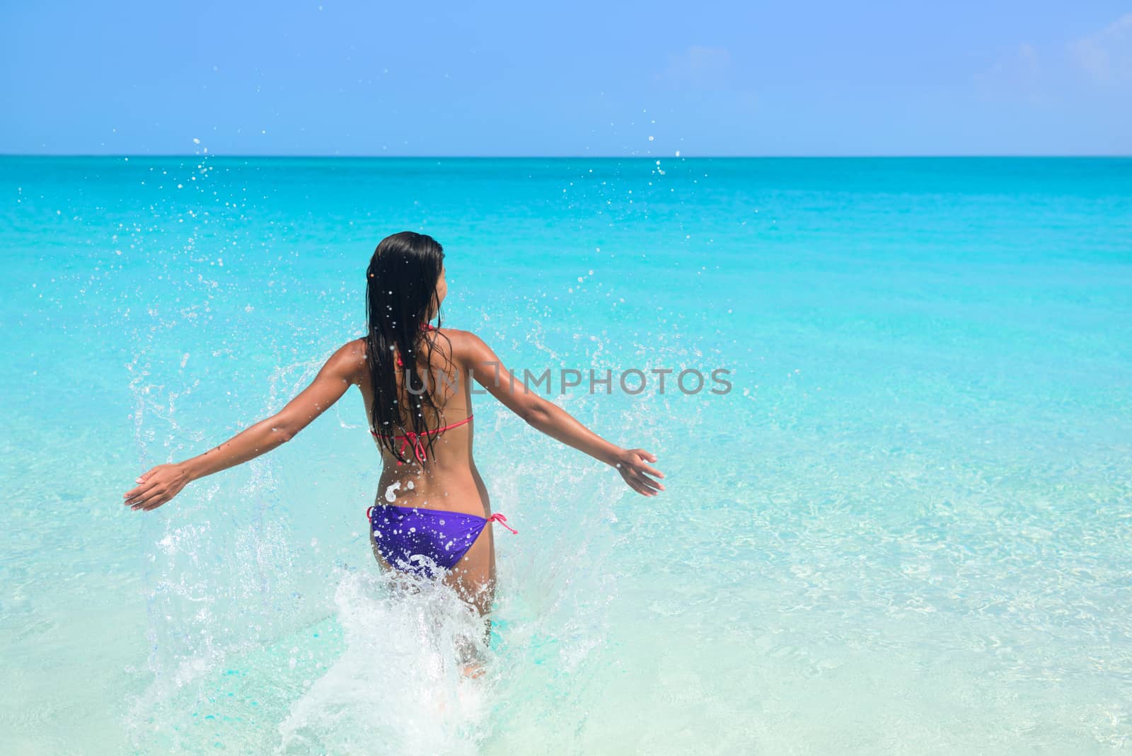 Beach vacation in tropical travel destination. Sexy woman in bikini feeling free swimming splashing water in blue ocean enjoying her sunny holidays. Concept of people having fun under the sun.