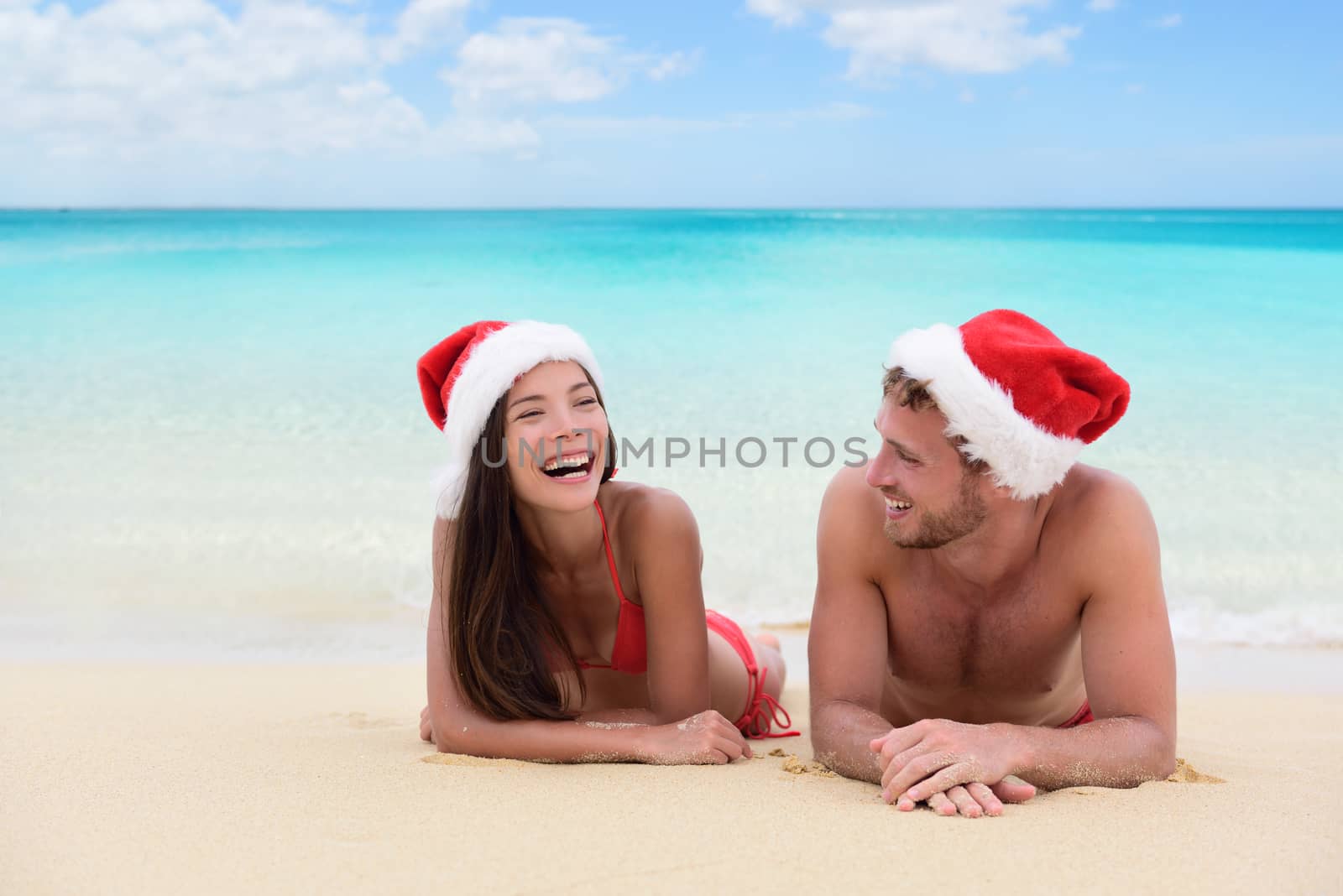 Christmas couple relaxing on beach winter vacation. Happy young adults friends or in love laughing on white sand in tropical travel destination for their new year holiday.