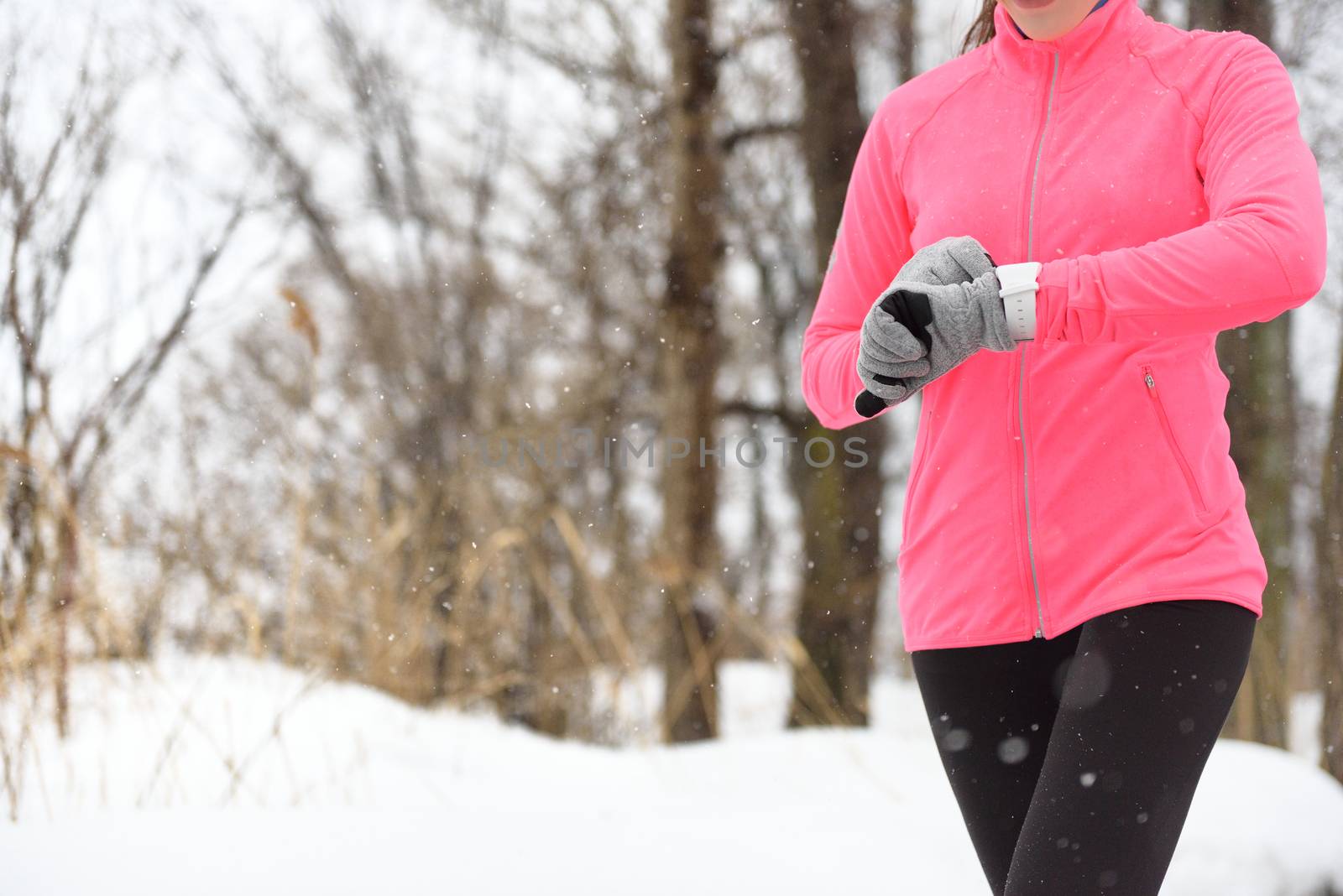 Runner using smartwatch jogging in snow trail in forest. winter weather closeup. Female athlete checking her cardio with a heart rate monitor during workout outside in running park.