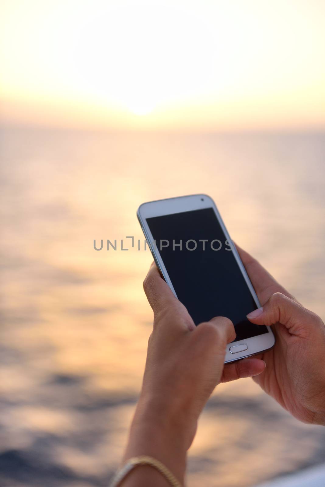 Smart phone close up - woman using smartphone app at ocean sunset at sea by the beach.
