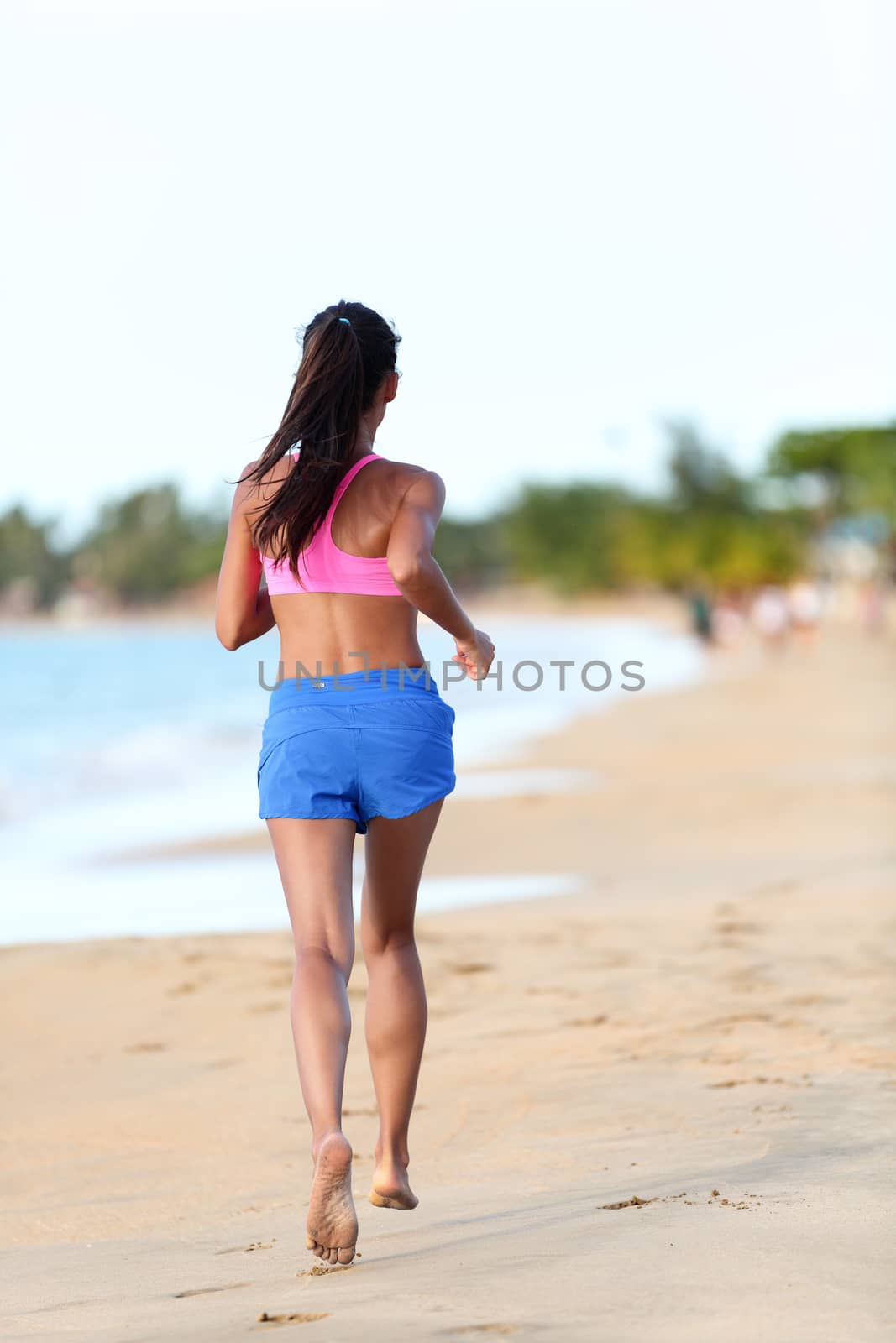 Young fit woman jogging on beach. Full length rear view of determined female is in sports clothing. Runner is exercising at sea shore during sunny day.