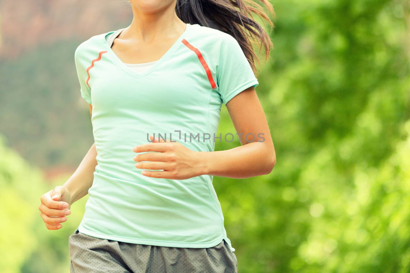 Running Woman Jogging. Midsection of determined woman runneron sunny day. Young female is in sports clothing. Sporty athlete runner is exercising against trees.